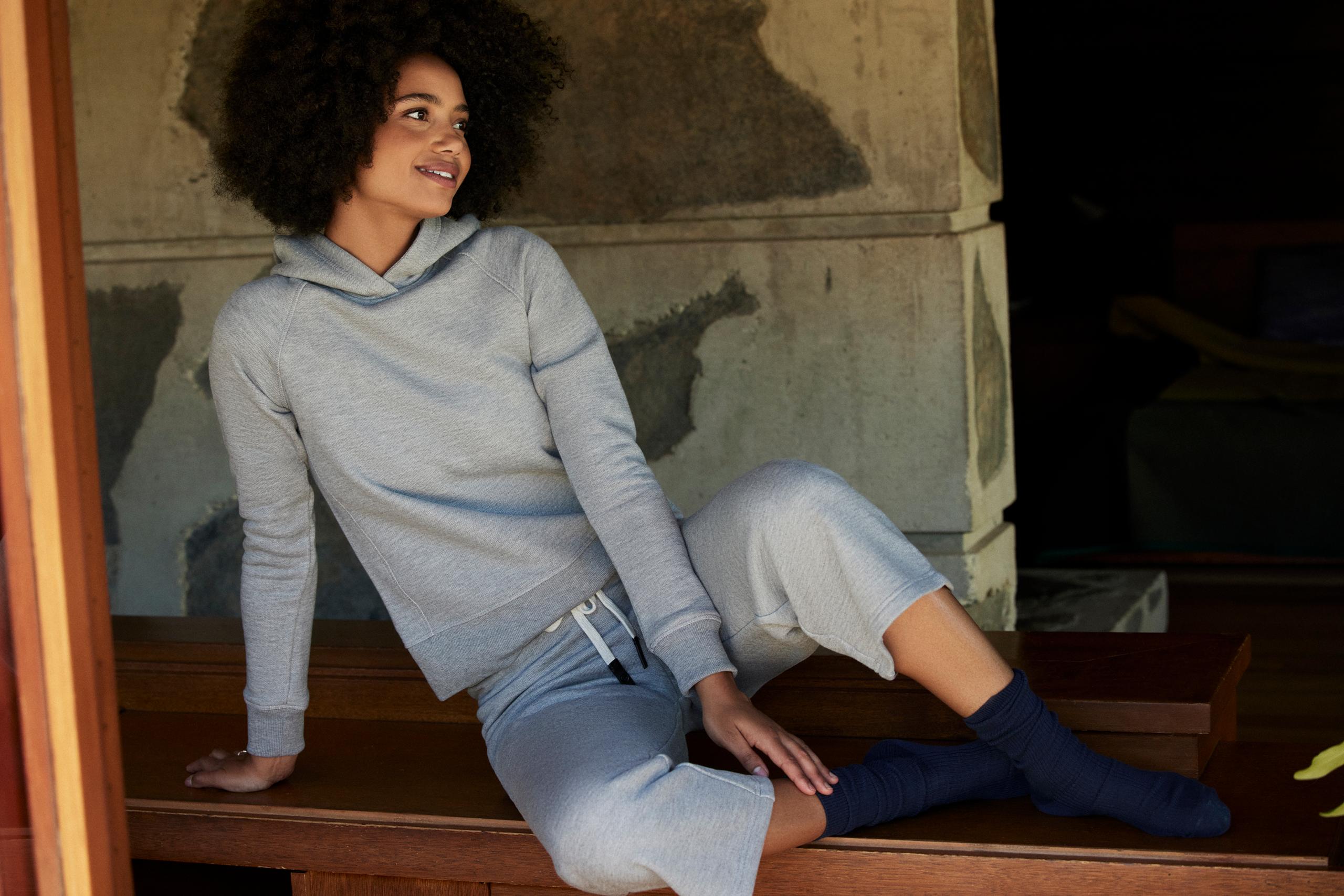 Woman wearing Foundation Hoodie and Foundation Cropped Pant sitting on wood cabinet in mid-century home