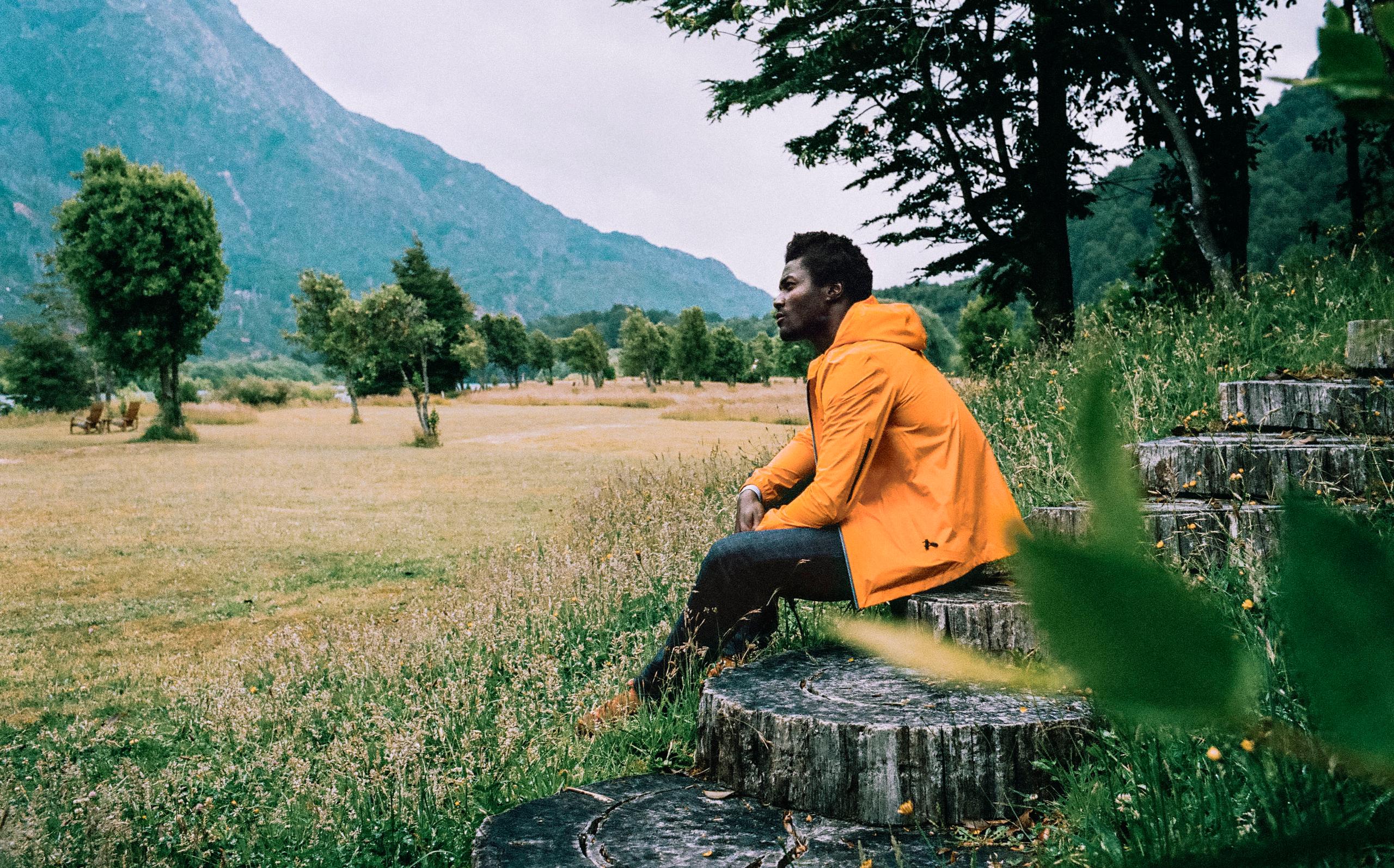 Man in orange jacket sitting on wood steps in front of field in Patagonia, Chile