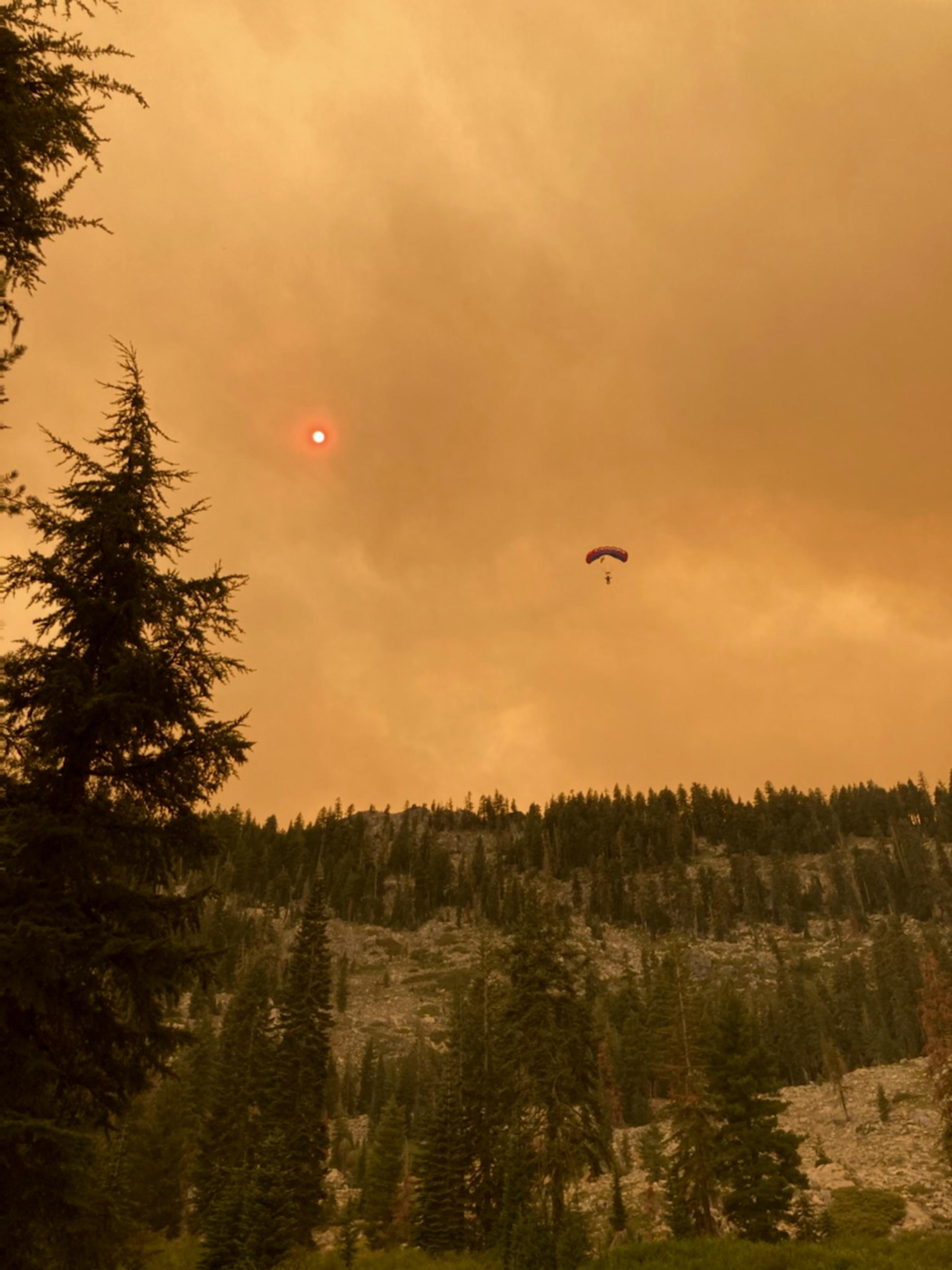 Smoke filled landscape with parachuting smokejumper midair in the distance