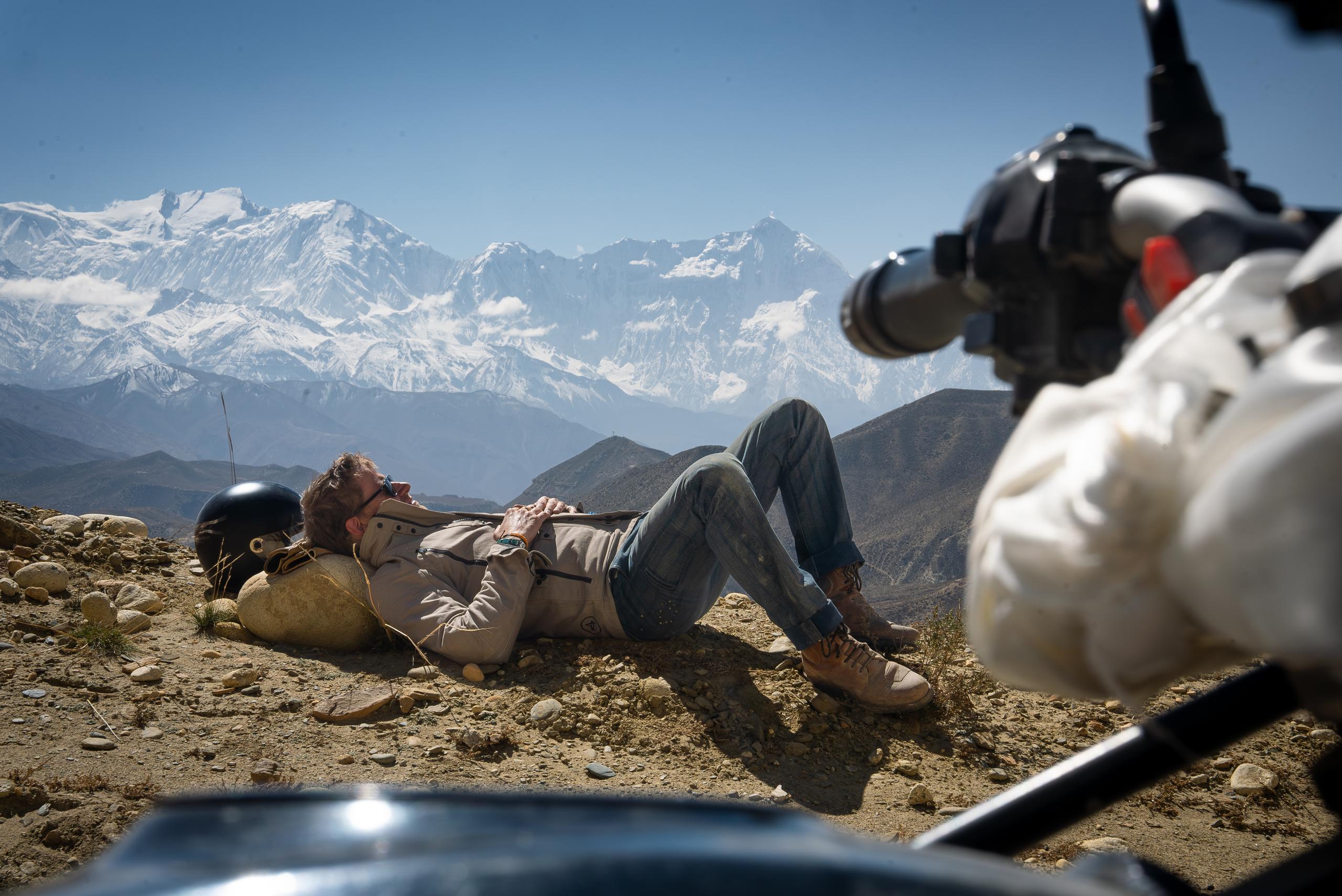 Motorcyclist laying down on rocks with snowy Himalayan mountains in the background