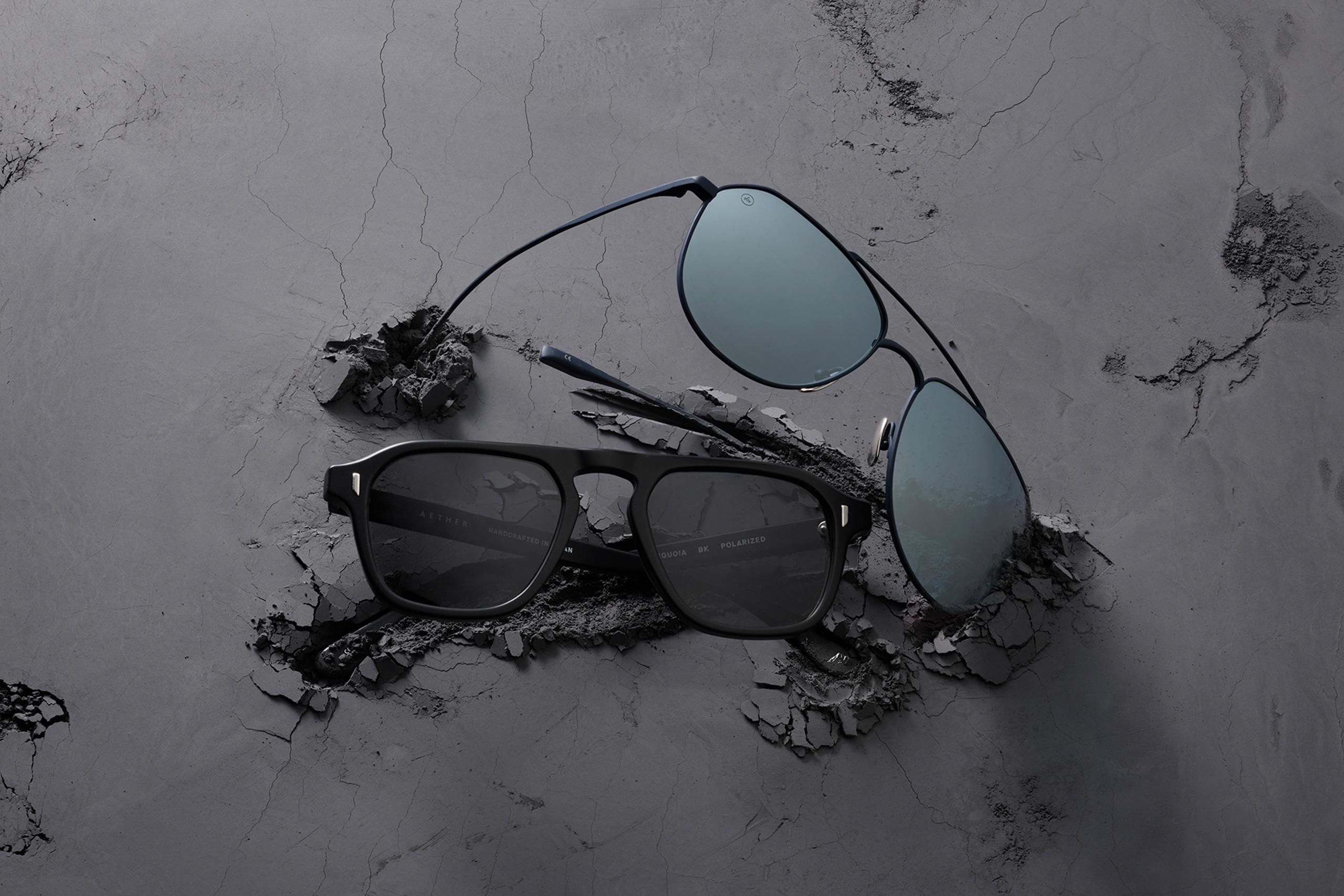 Still life of two AETHER sunglasses on black textured concrete