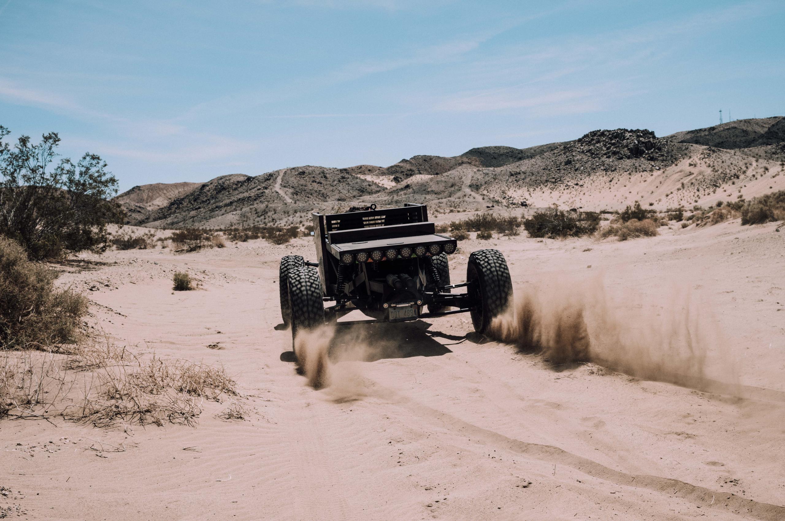 Custom black vehicle driving through desert kicking up sand
