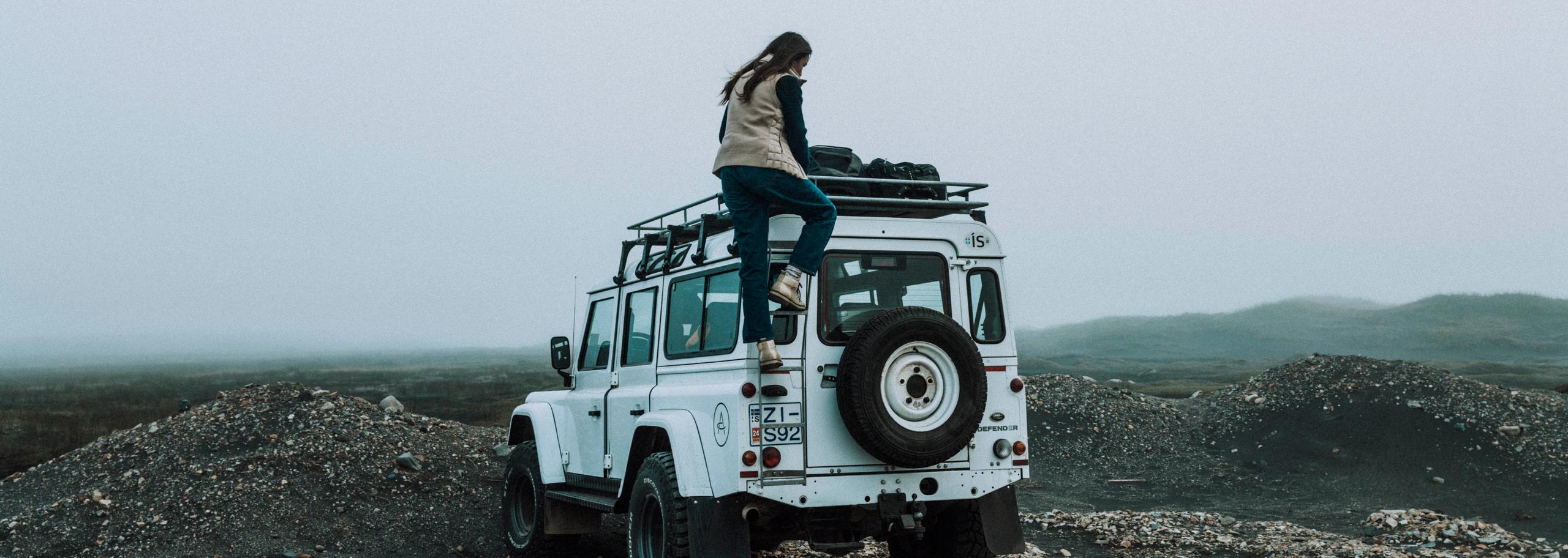 Woman stepping up to roof of white Defender truck in Iceland landscape
