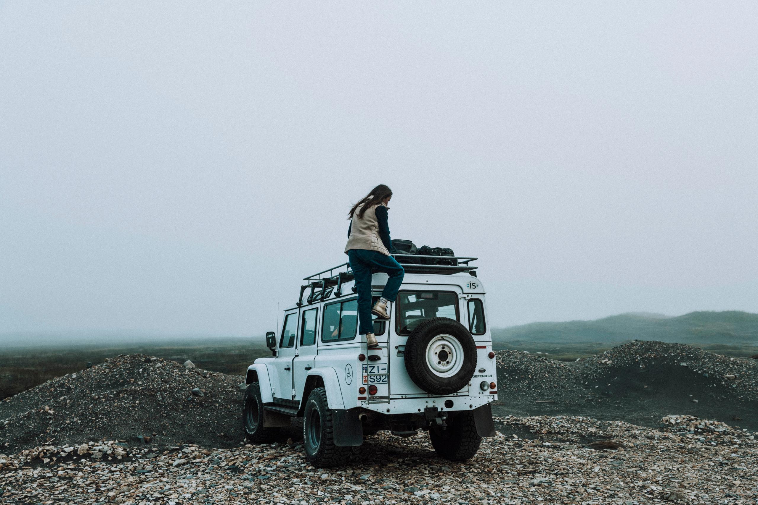Julia wearing Phase Vest climbing on top of a Defender 110.