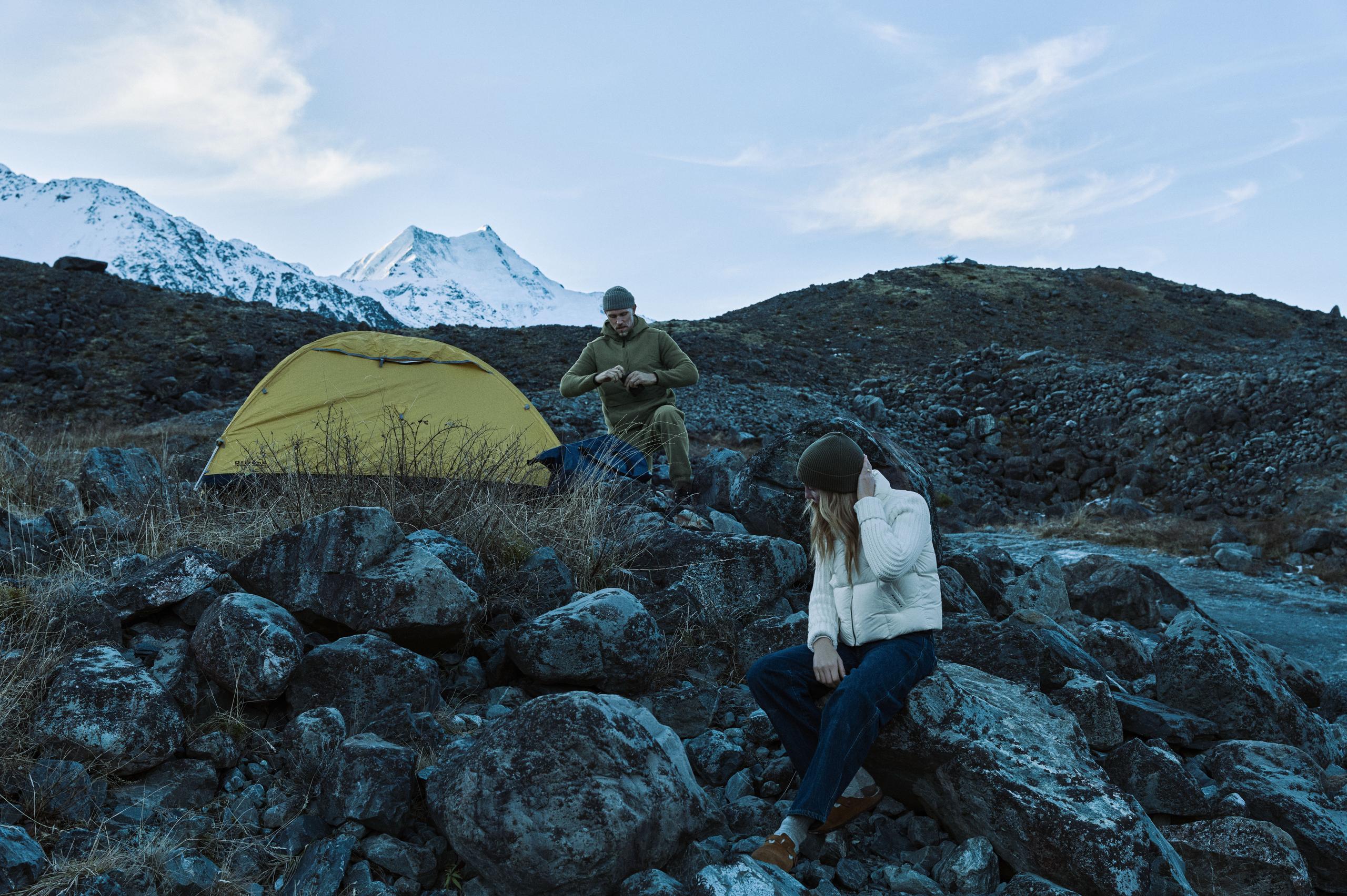 A man and a woman stationed a camping tent near some rocks