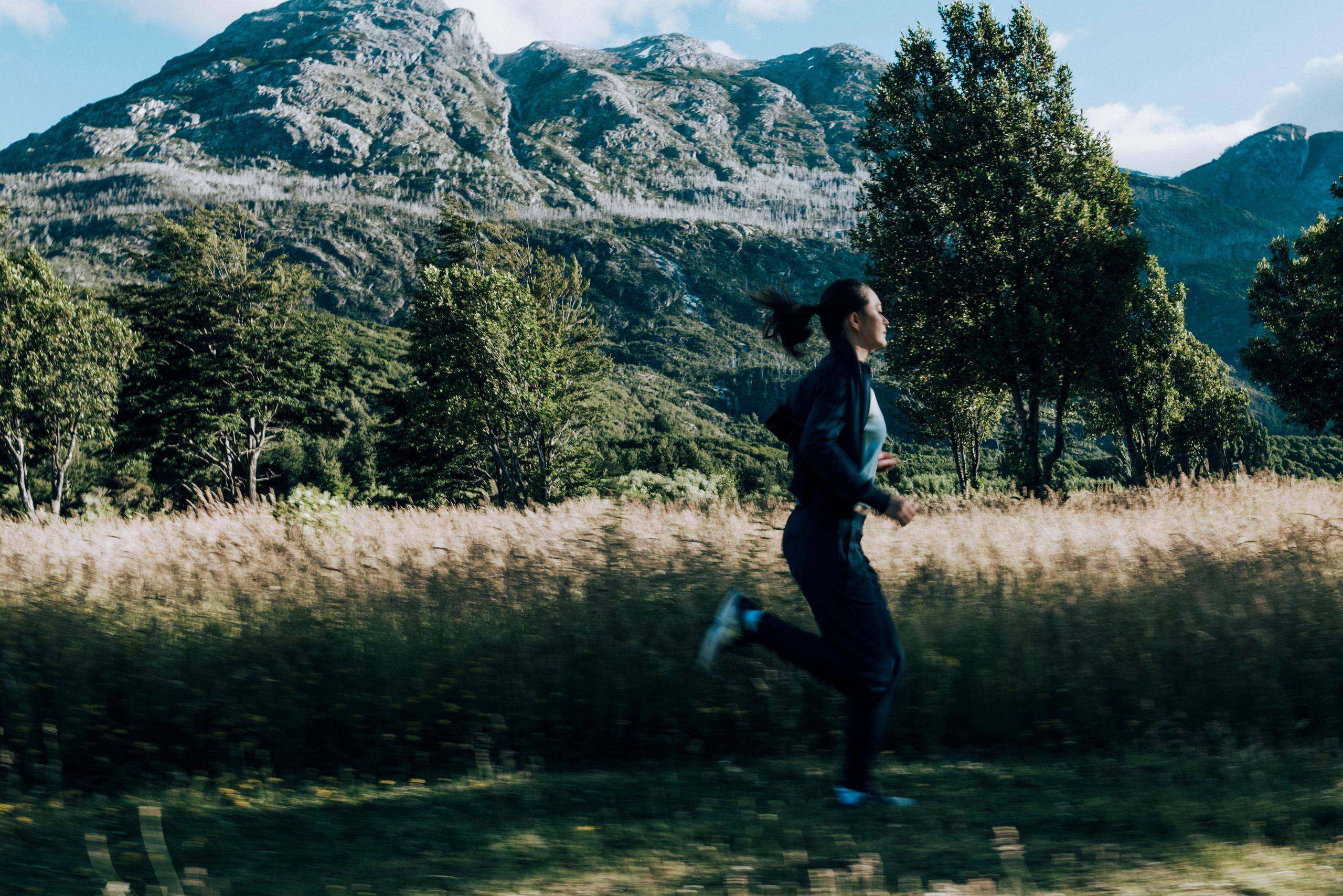 Woman running in field with Patagonia mountains in the background