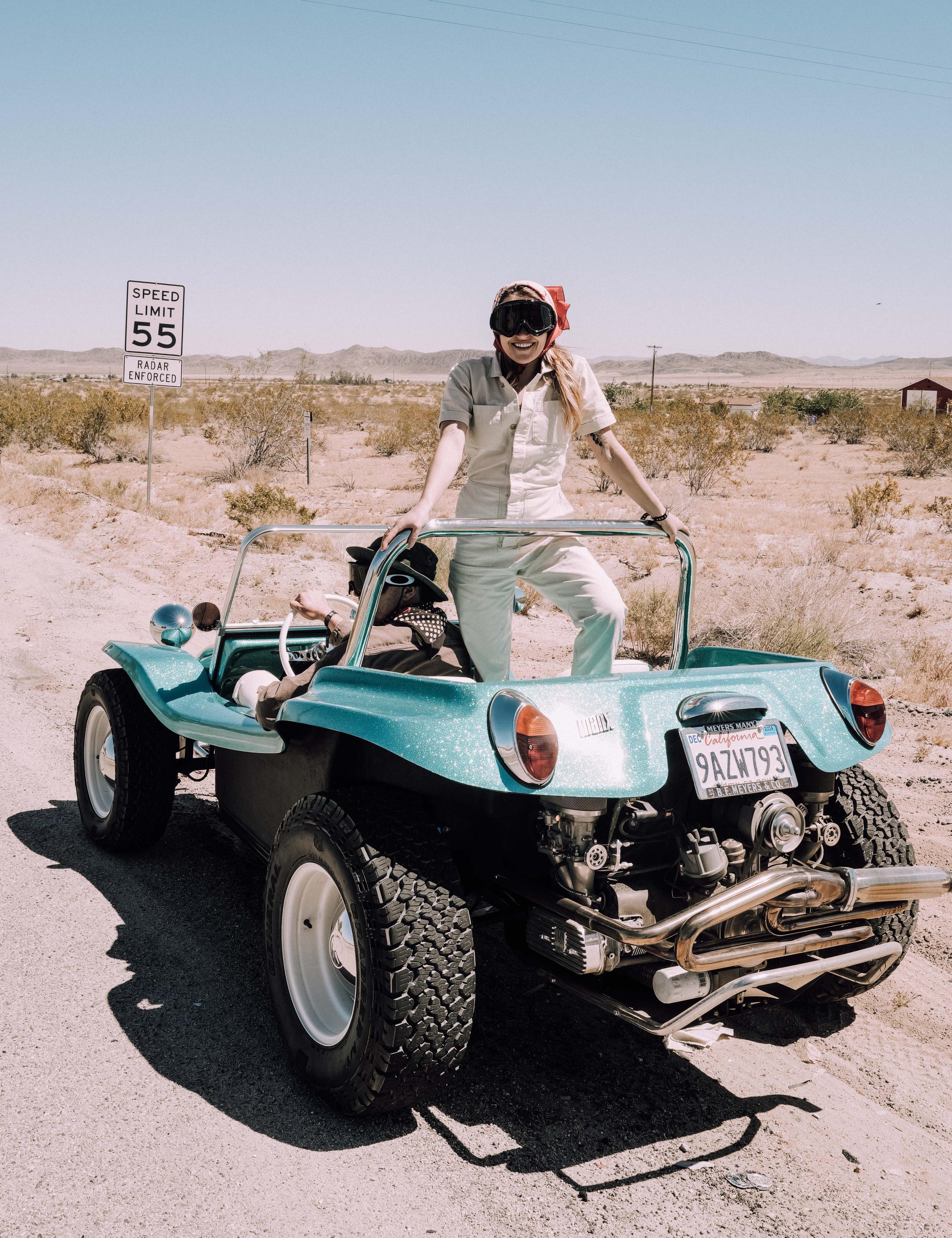 Woman standing on the back of a custom vehicle on a dirt road in Joshua Tree, California
