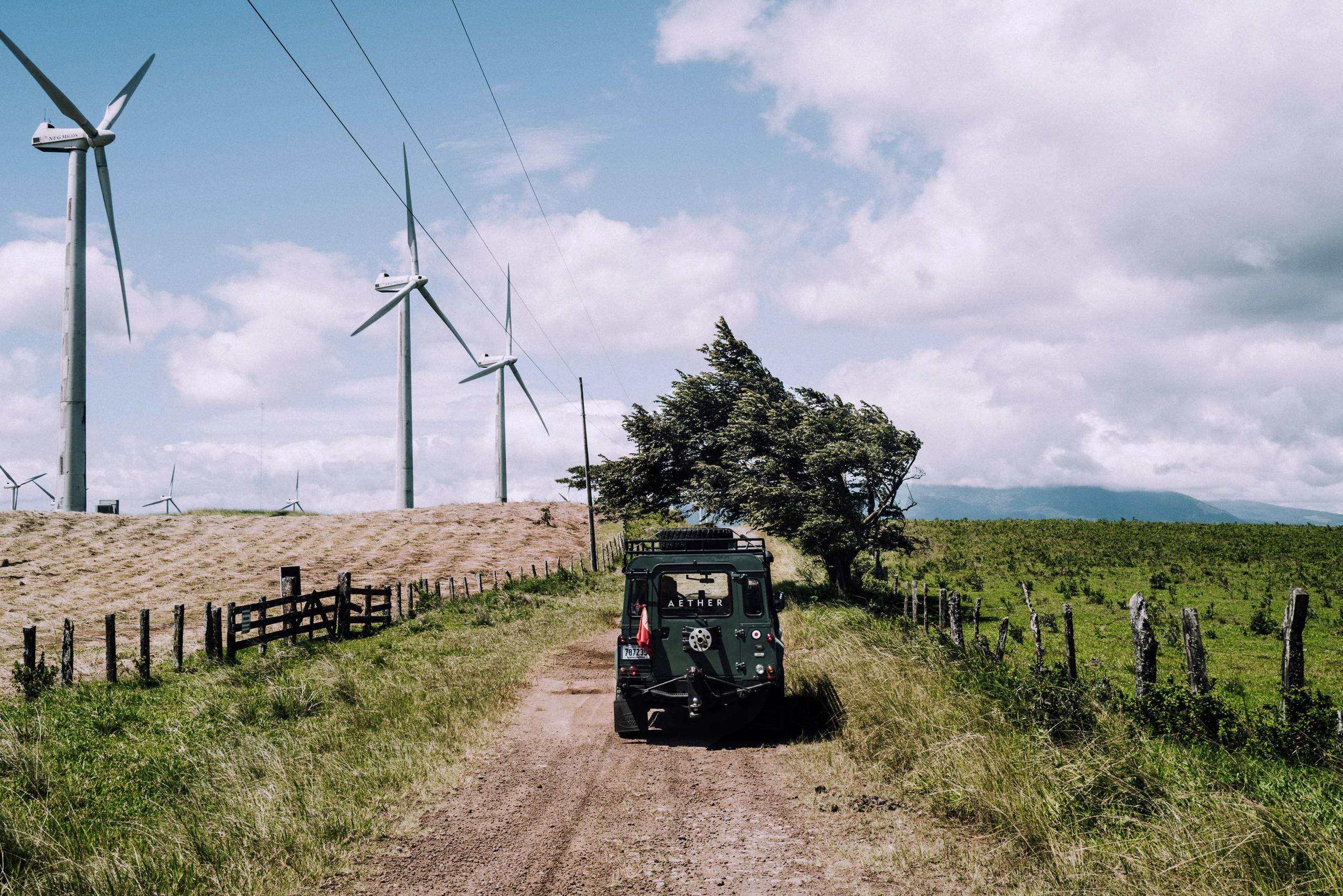 Vintage Land Rover on gravel country road with windmills in background in Costa Rica