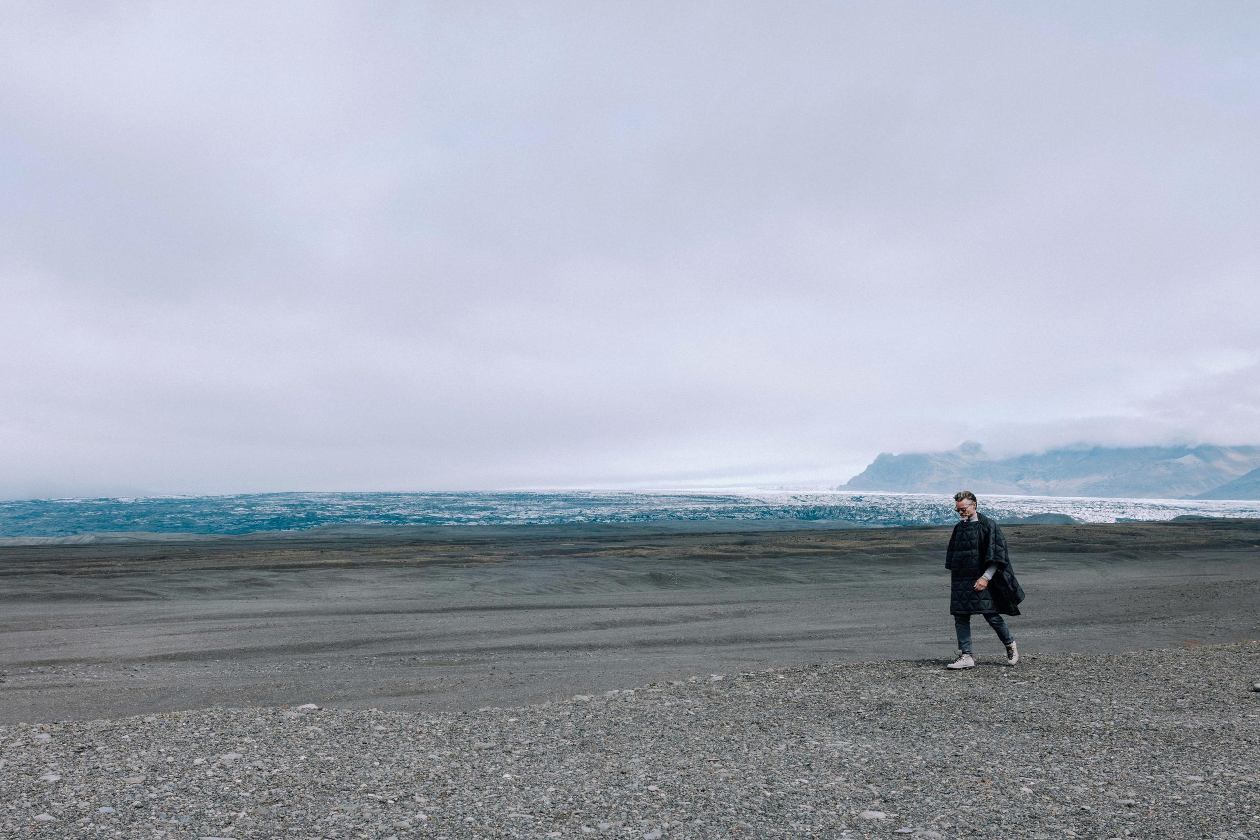 Man walking on dark rocky terrain next to glacier in Iceland