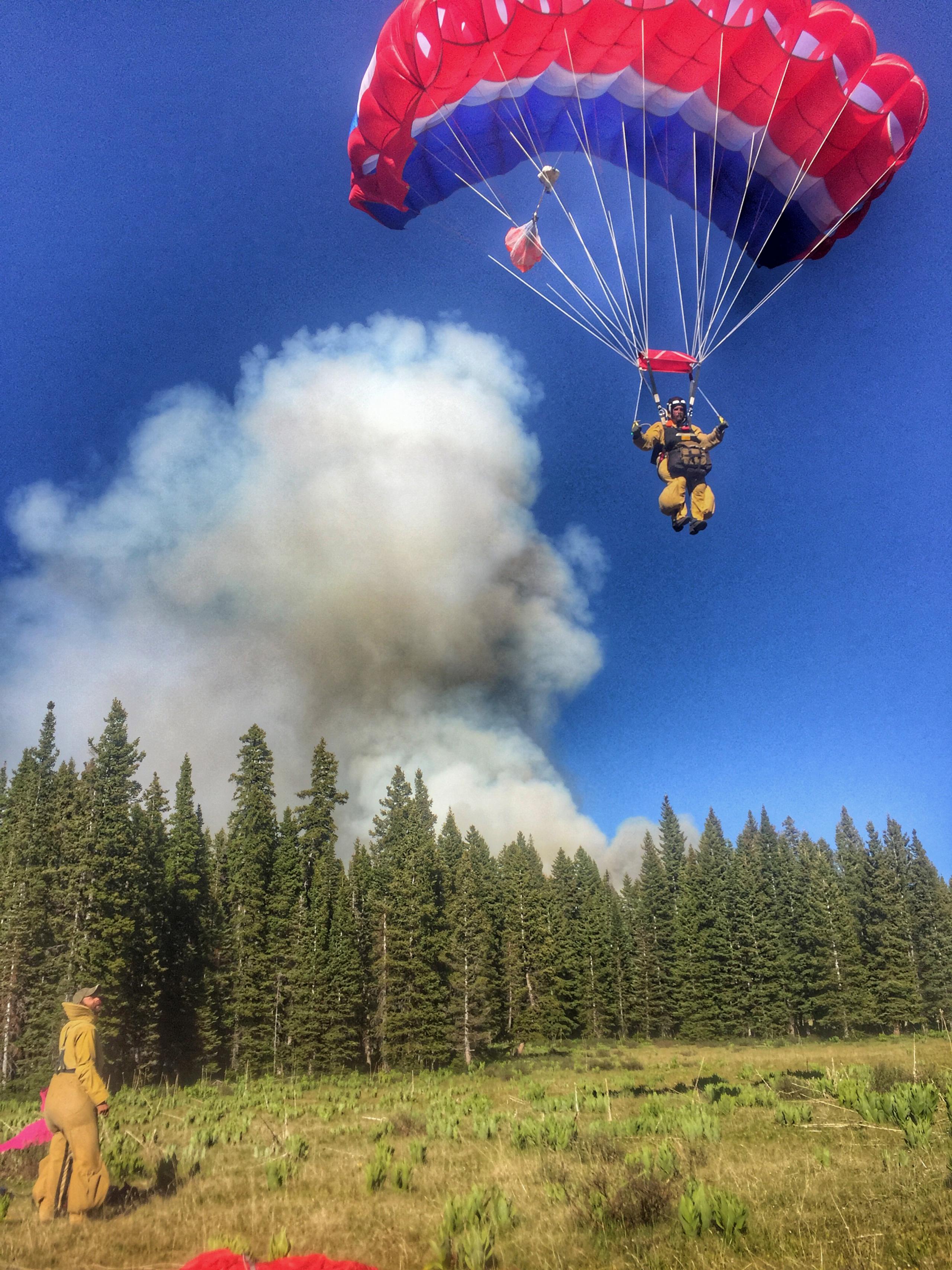 Smokejumper parachuting into a field with giant plume of smoke in the background