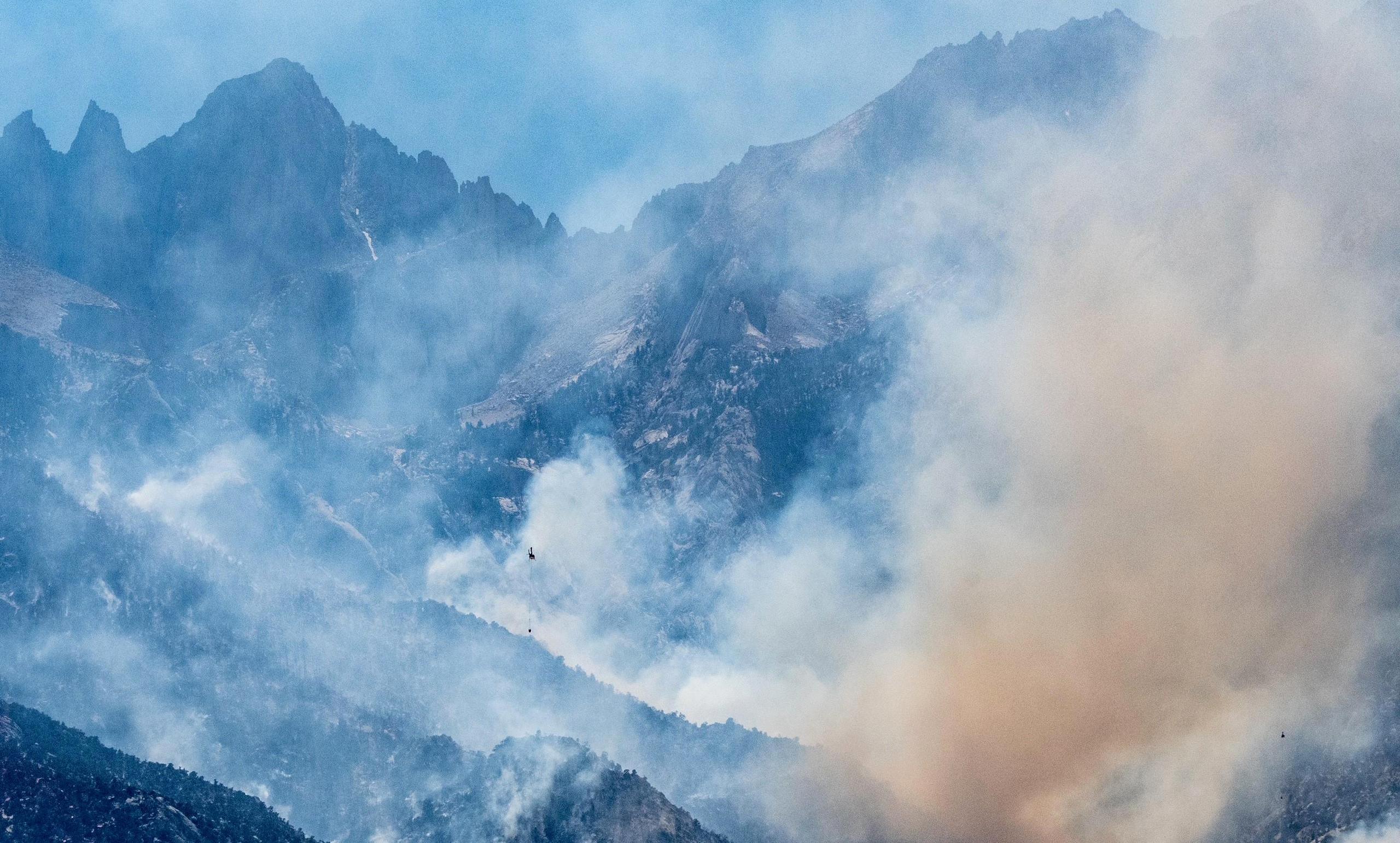 Smoking rising from canyons during Inyo Creek Fire with small helicopter seen in the distance