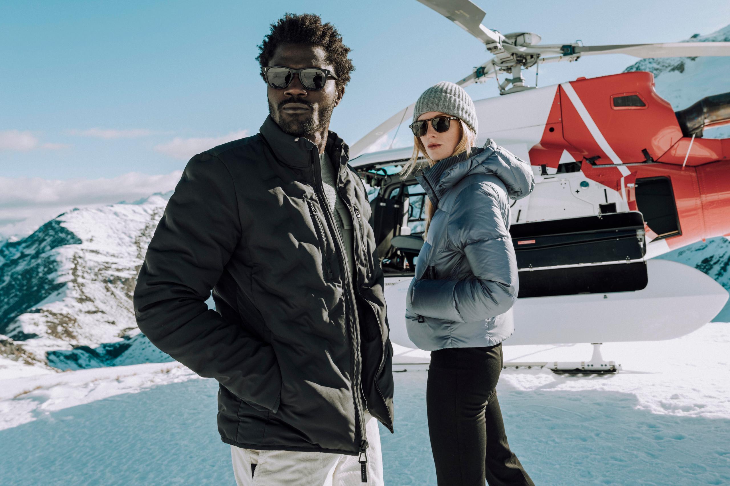 Men and women looking afar in front of a helicopter on a snow mountain.