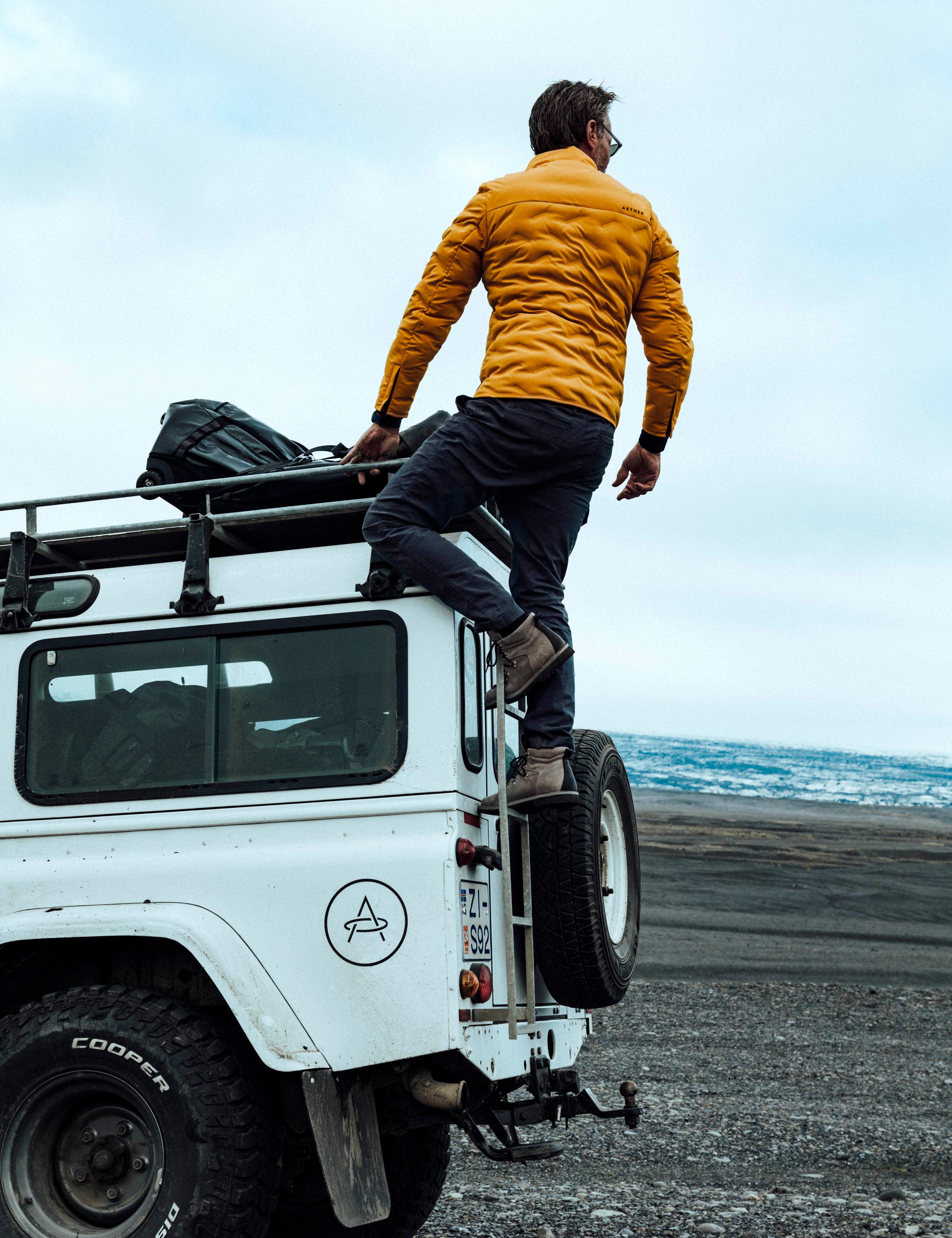 Man in the Rex Jacket standing on back of white Defender in Iceland black sand beach