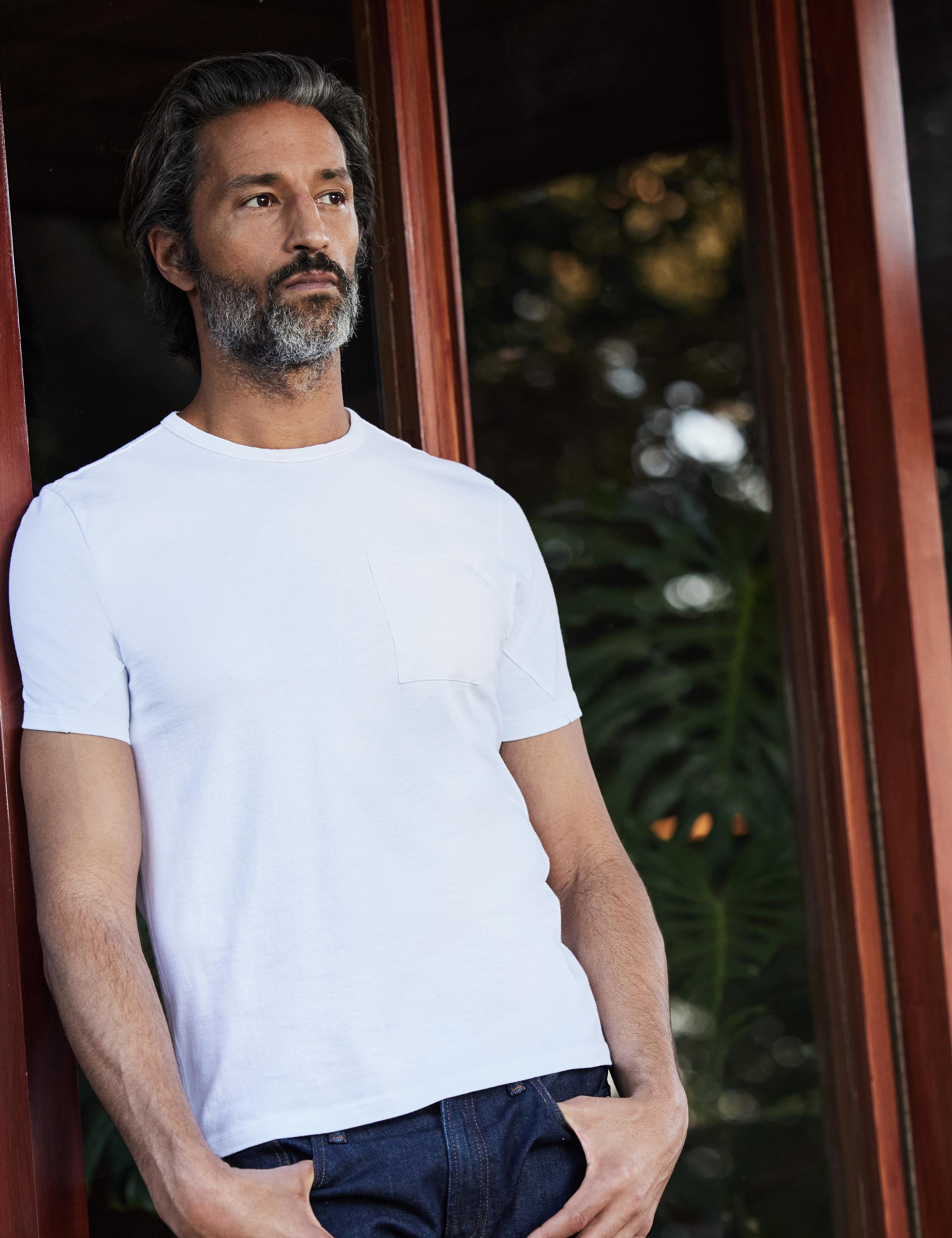 Man wearing Laurentic Crew Tee leaning on patio windows of mid-century home