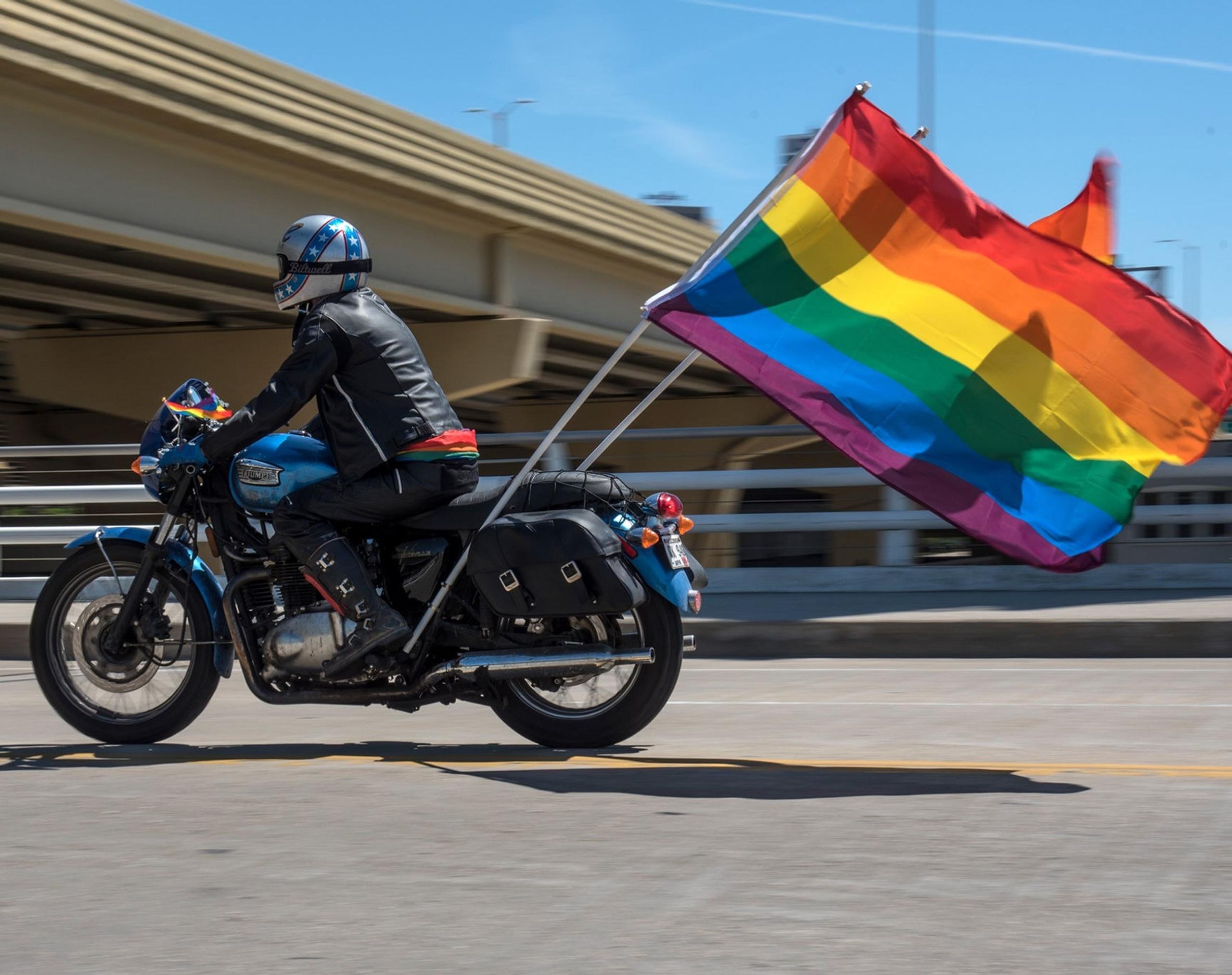 Motorcyclist on highway with two Pride flags flying from the back