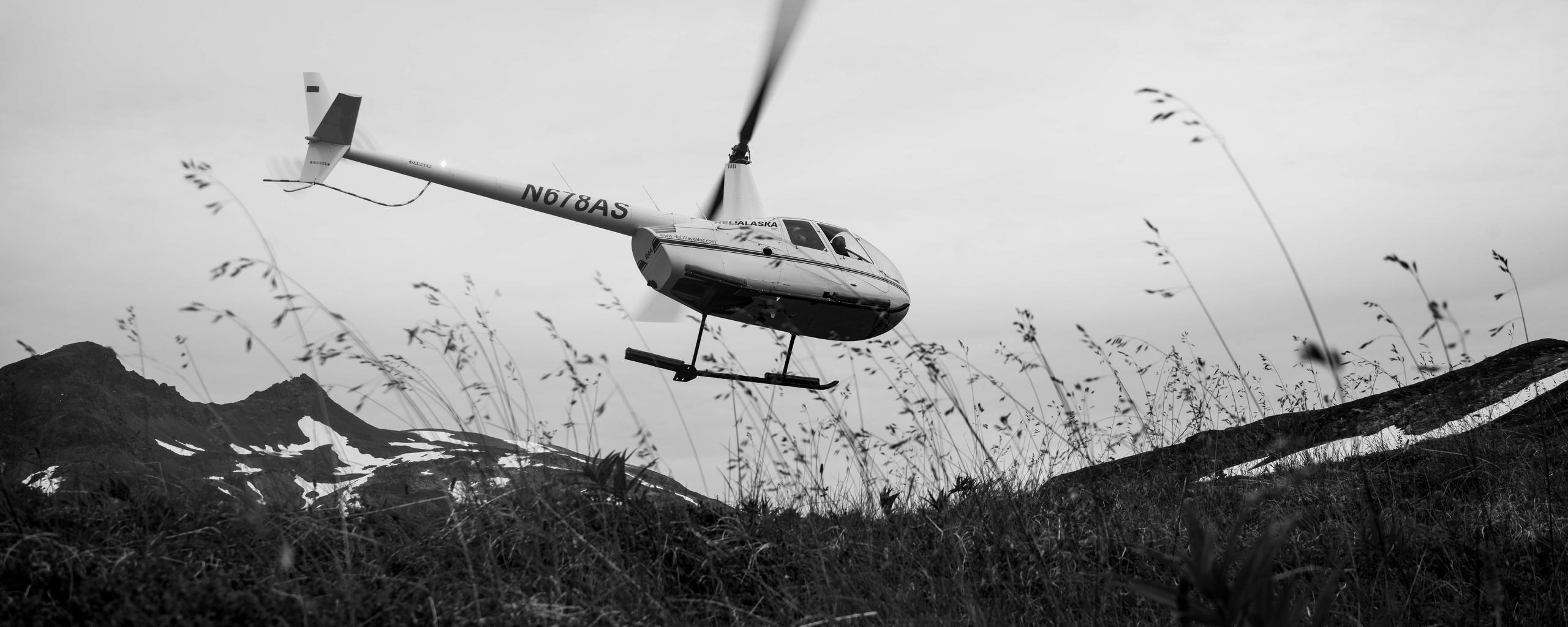 Black and white photograph of helicopter taking off from Alaskan highlands