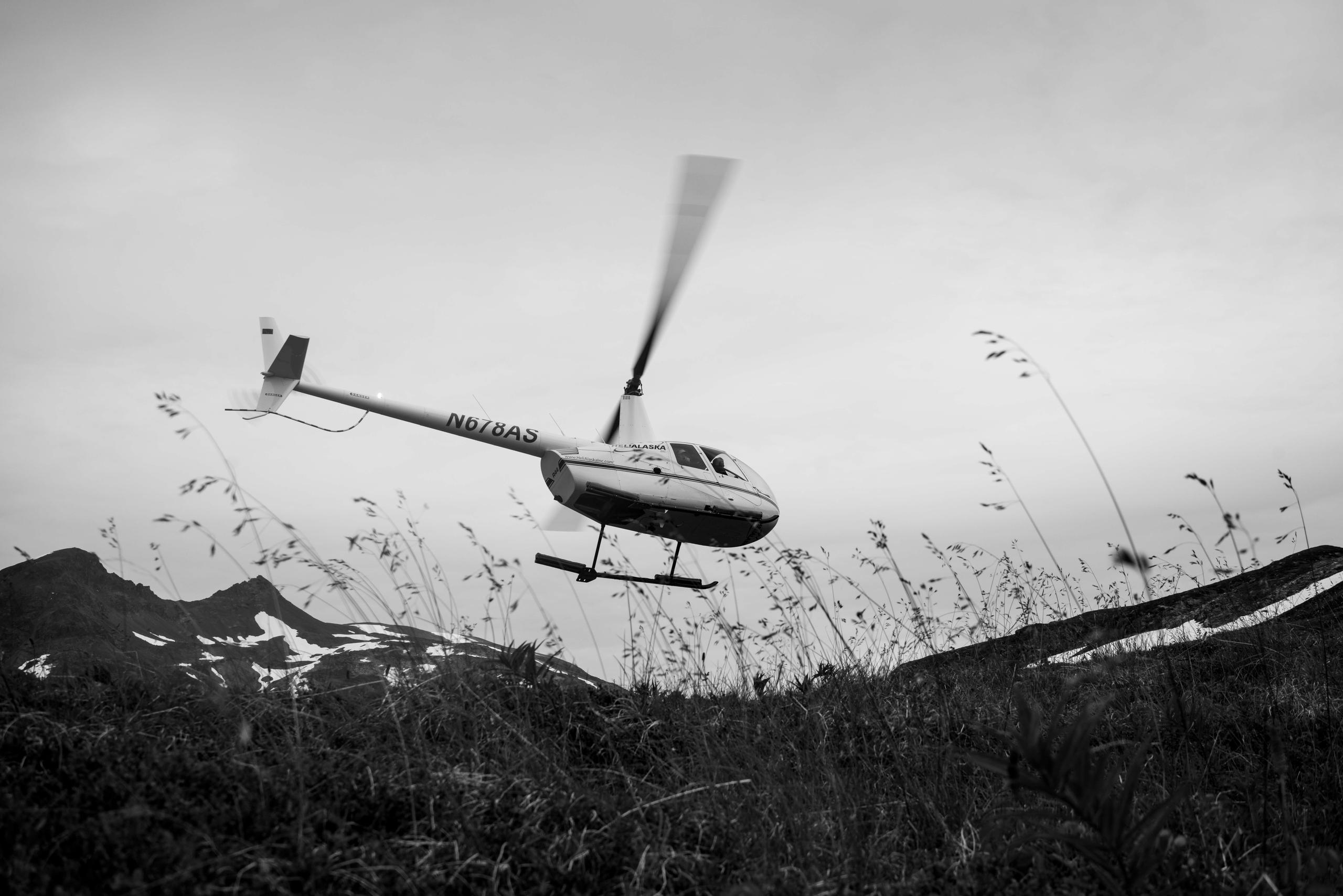 Black and white photo of helicopter taking off from Alaska landscape