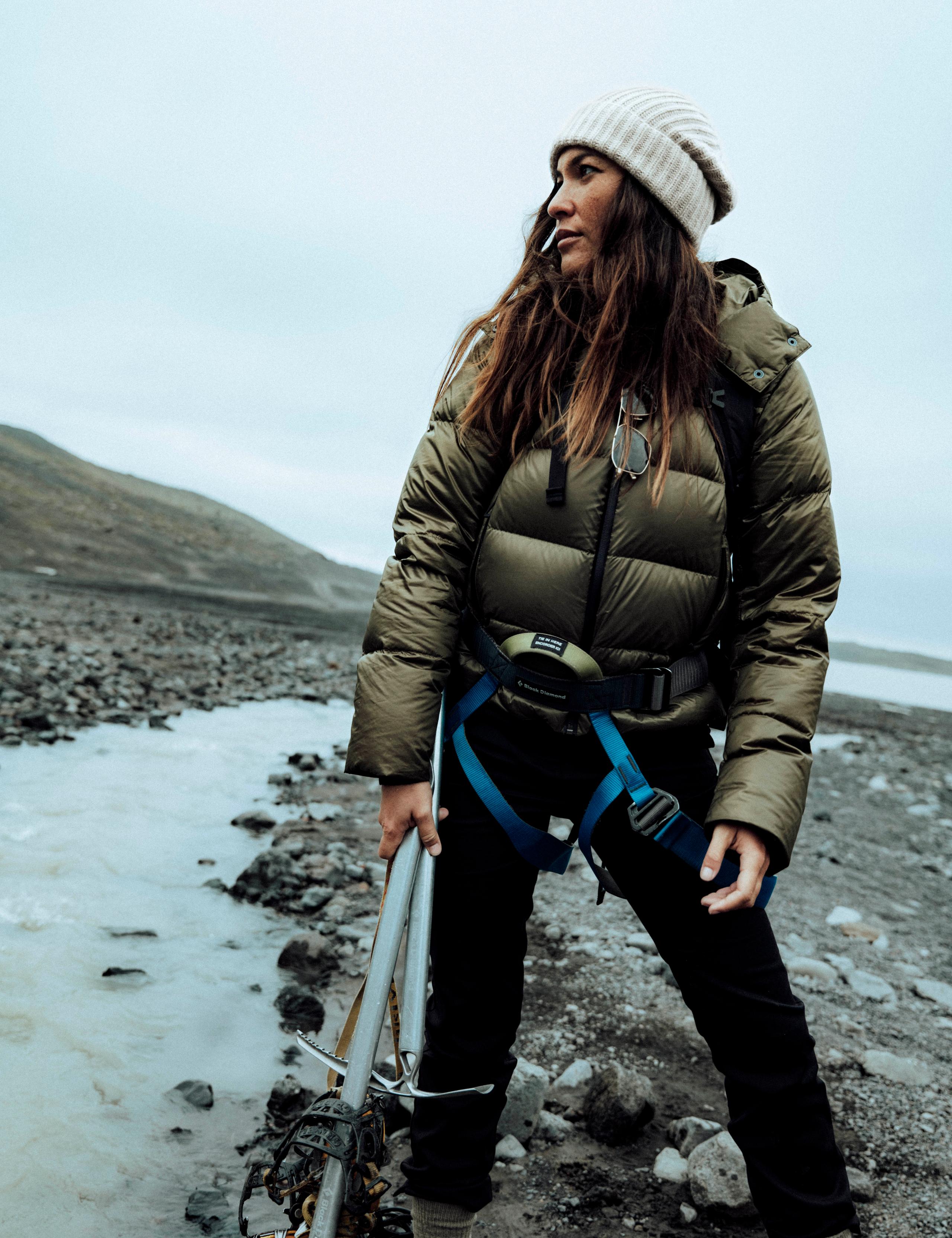 Woman in Aura Puffer Jacket with ice hiking gear in hand on Iceland beach