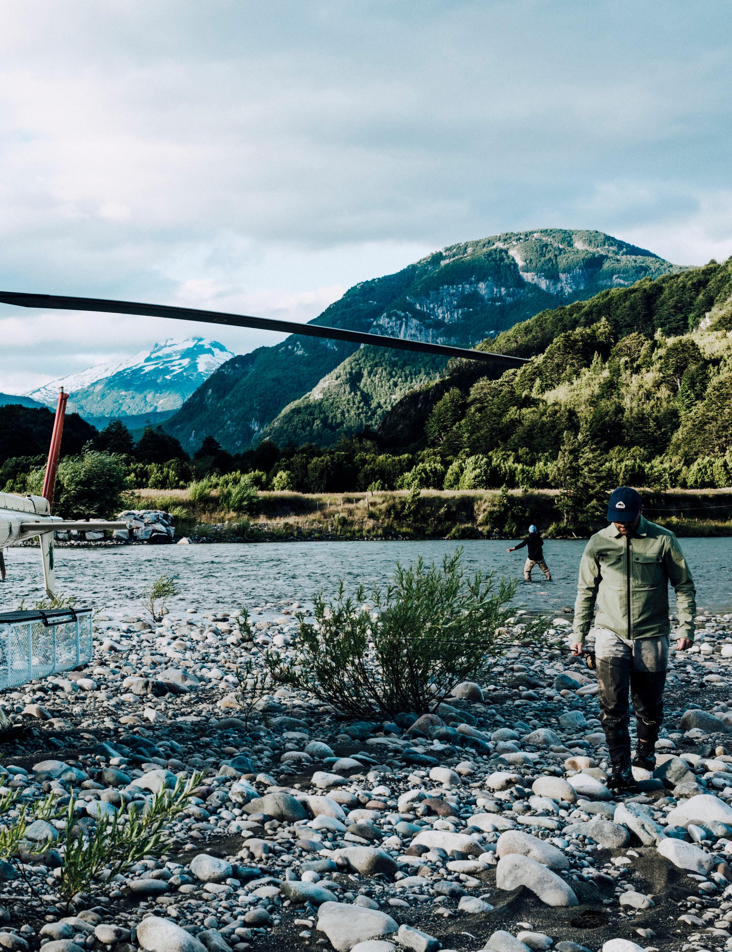 Man walking on rocky shore alongside river in Patagonia with helicopter parked nearby