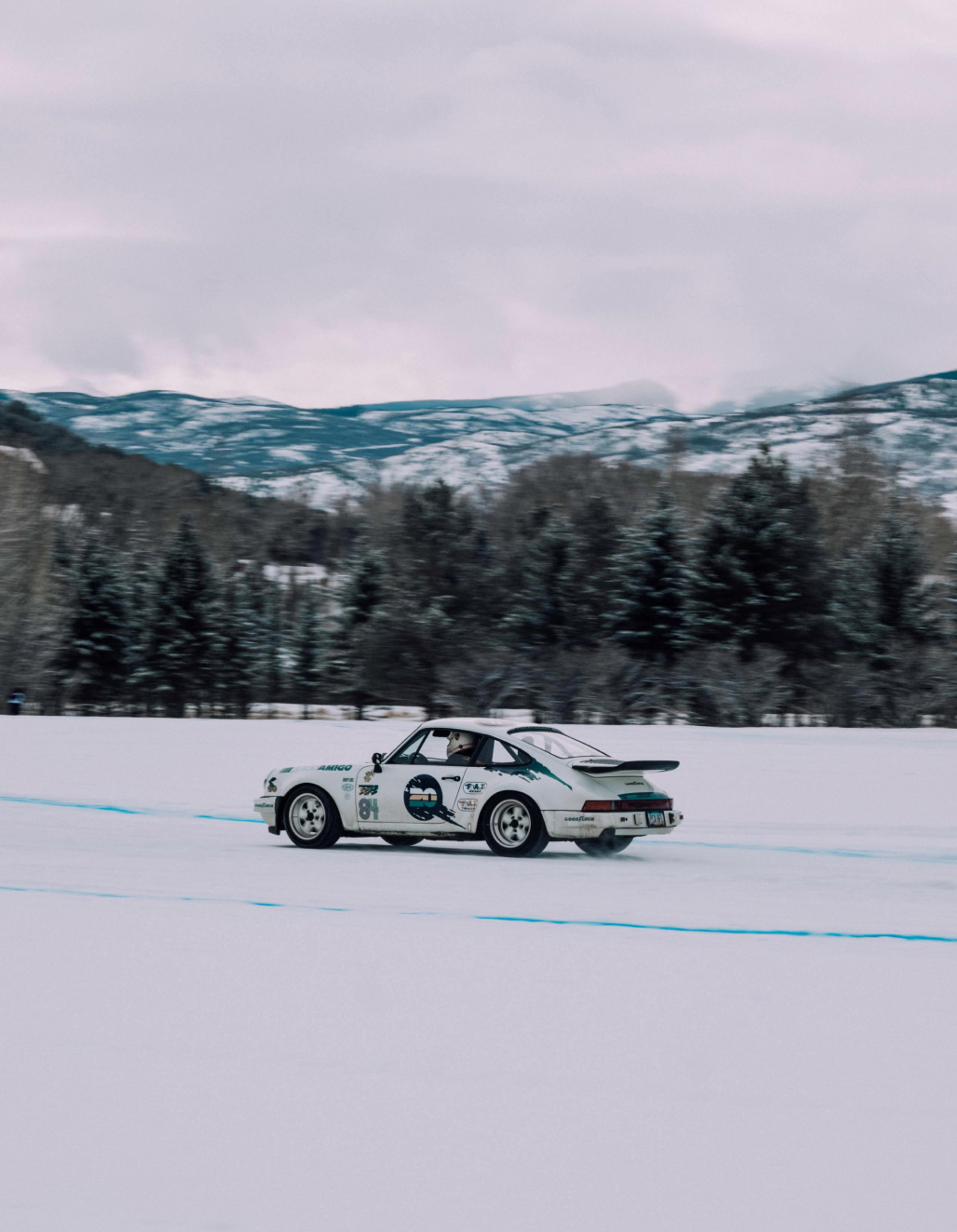 White Porsche 911 driving on ice track with mountains in the background
