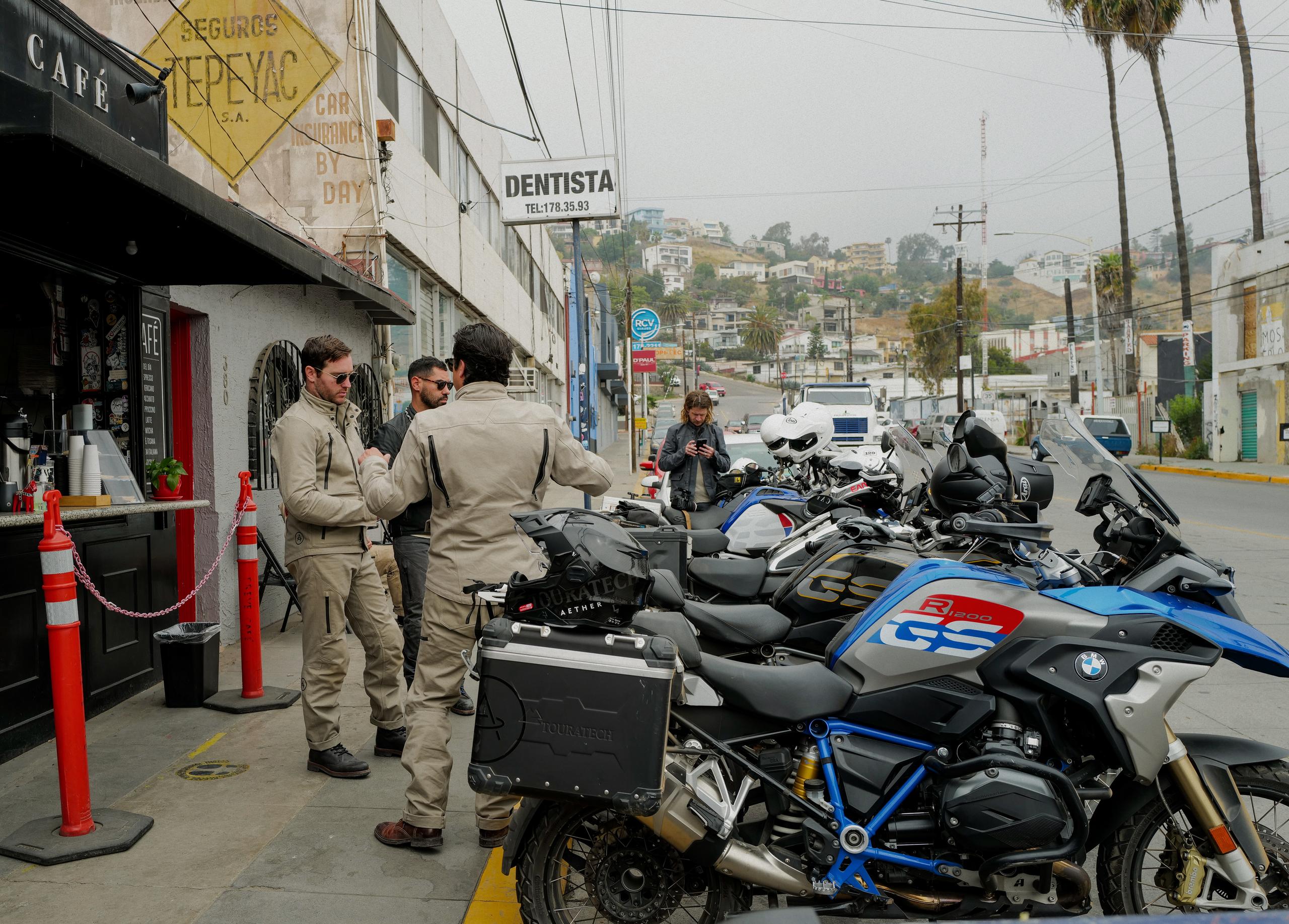 Motorcyclists standing on sidewalk next to motorcycles in city street of Ensenada