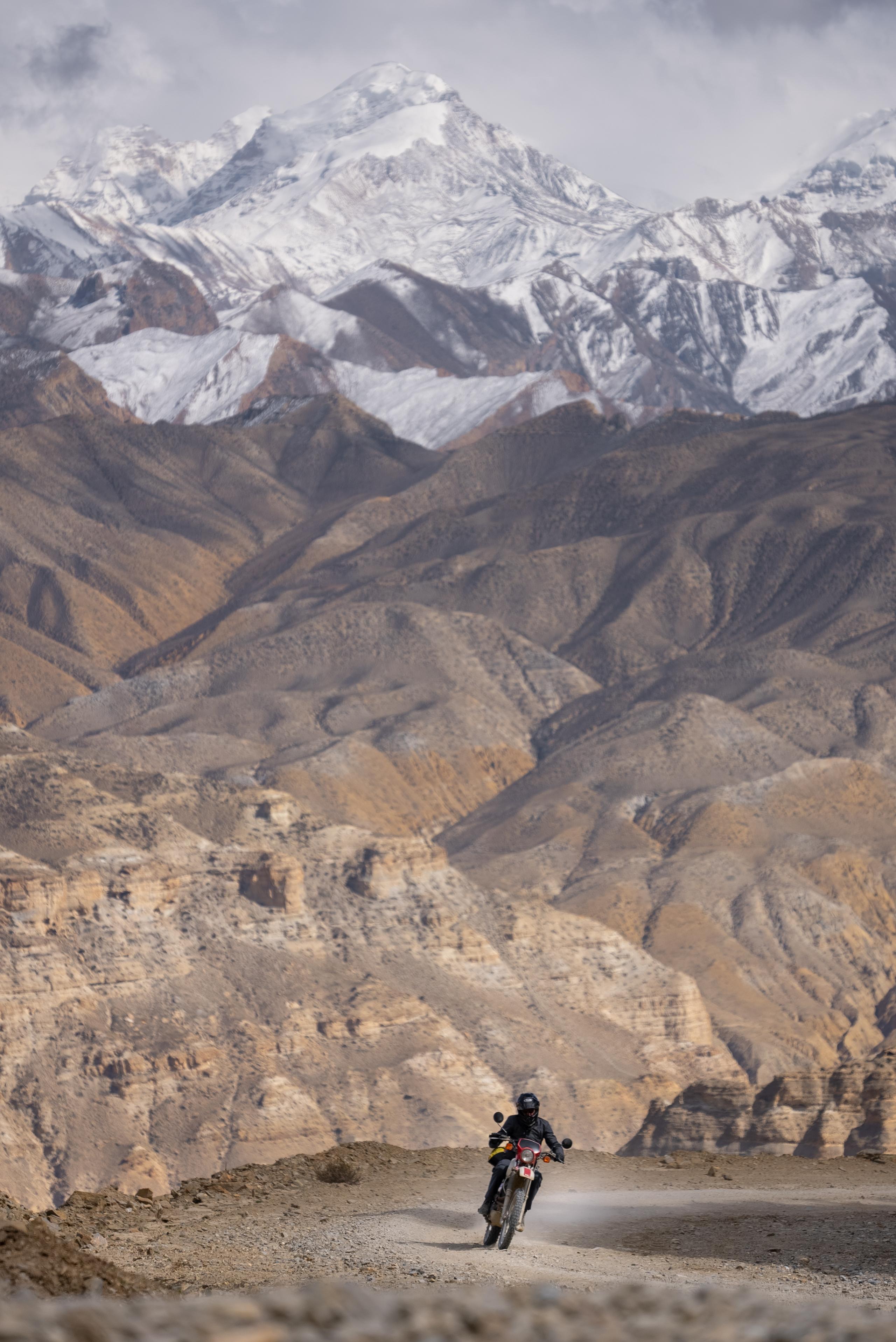 Motorcyclist riding on mountain dirt road with snowy Himalayan mountains in background