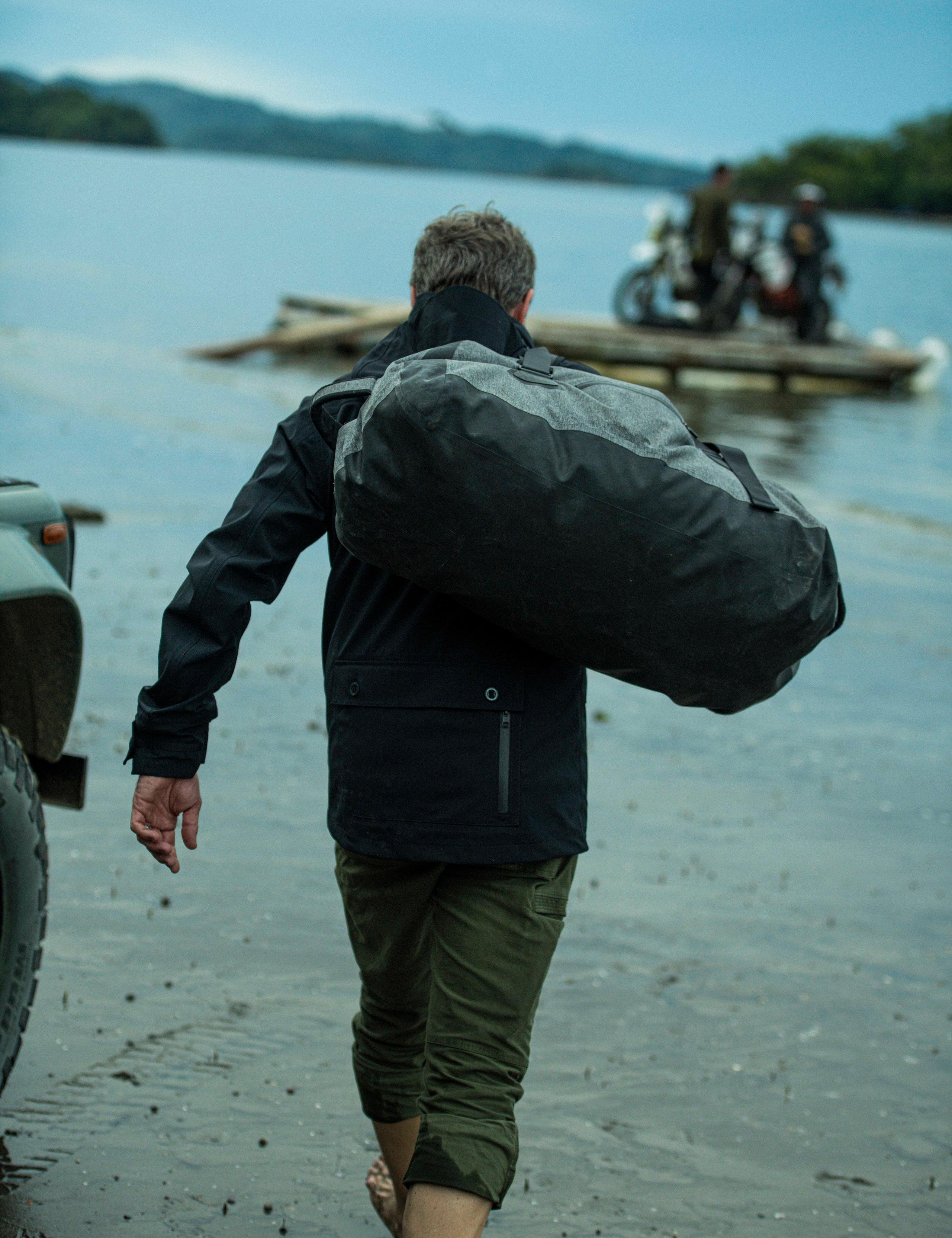 Man wearing Endeavor Jacket and holding a bag heading to transport raft on river in Costa Rica