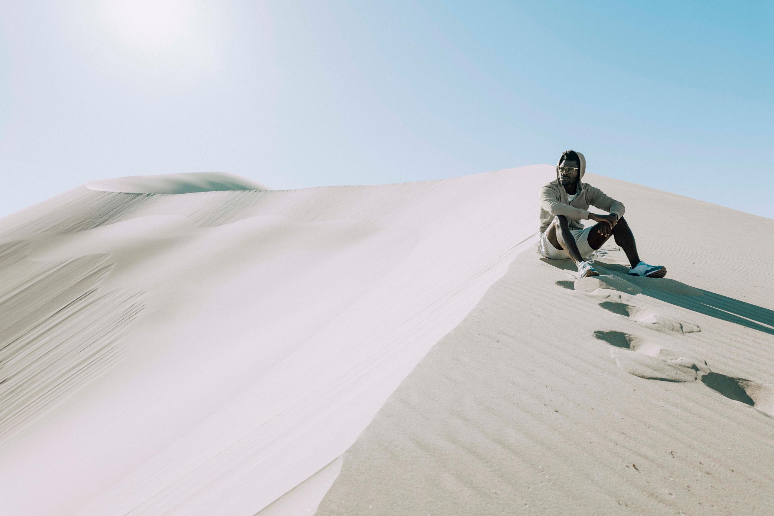 Man wearing Yosemite sunglasses sitting on desert sand dune