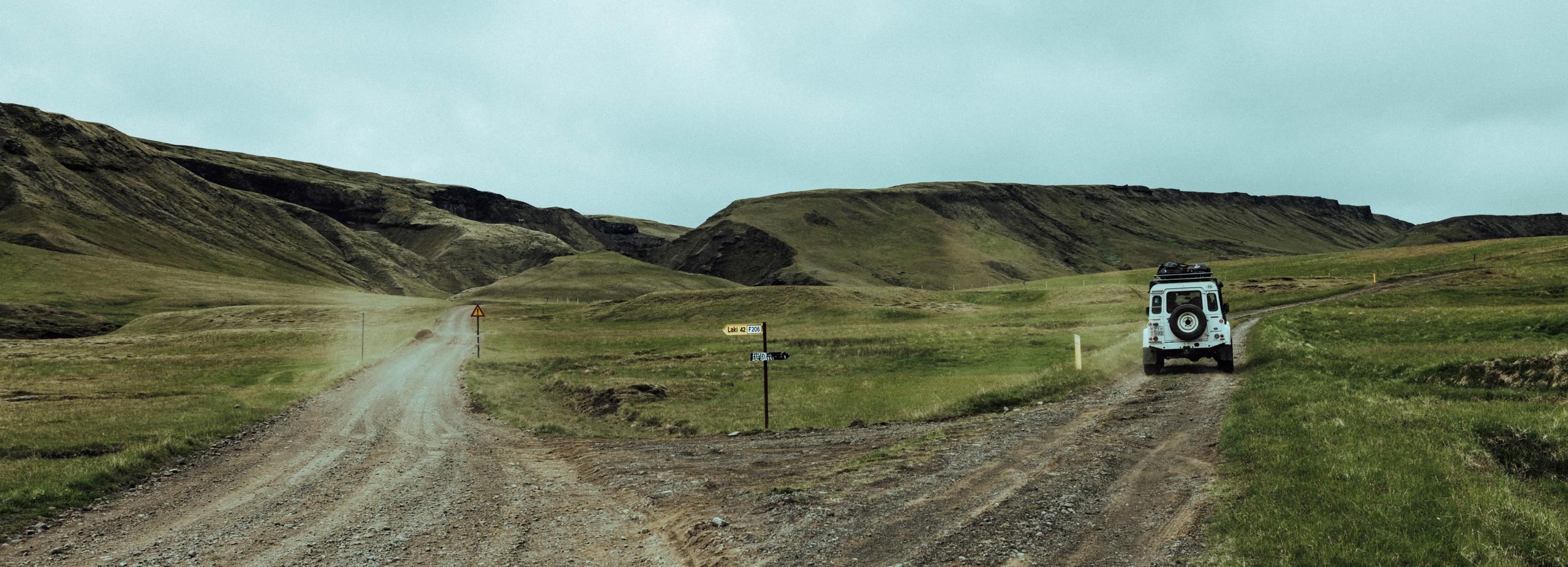 White Defender truck driving down the right side of a forked gravel road in Iceland