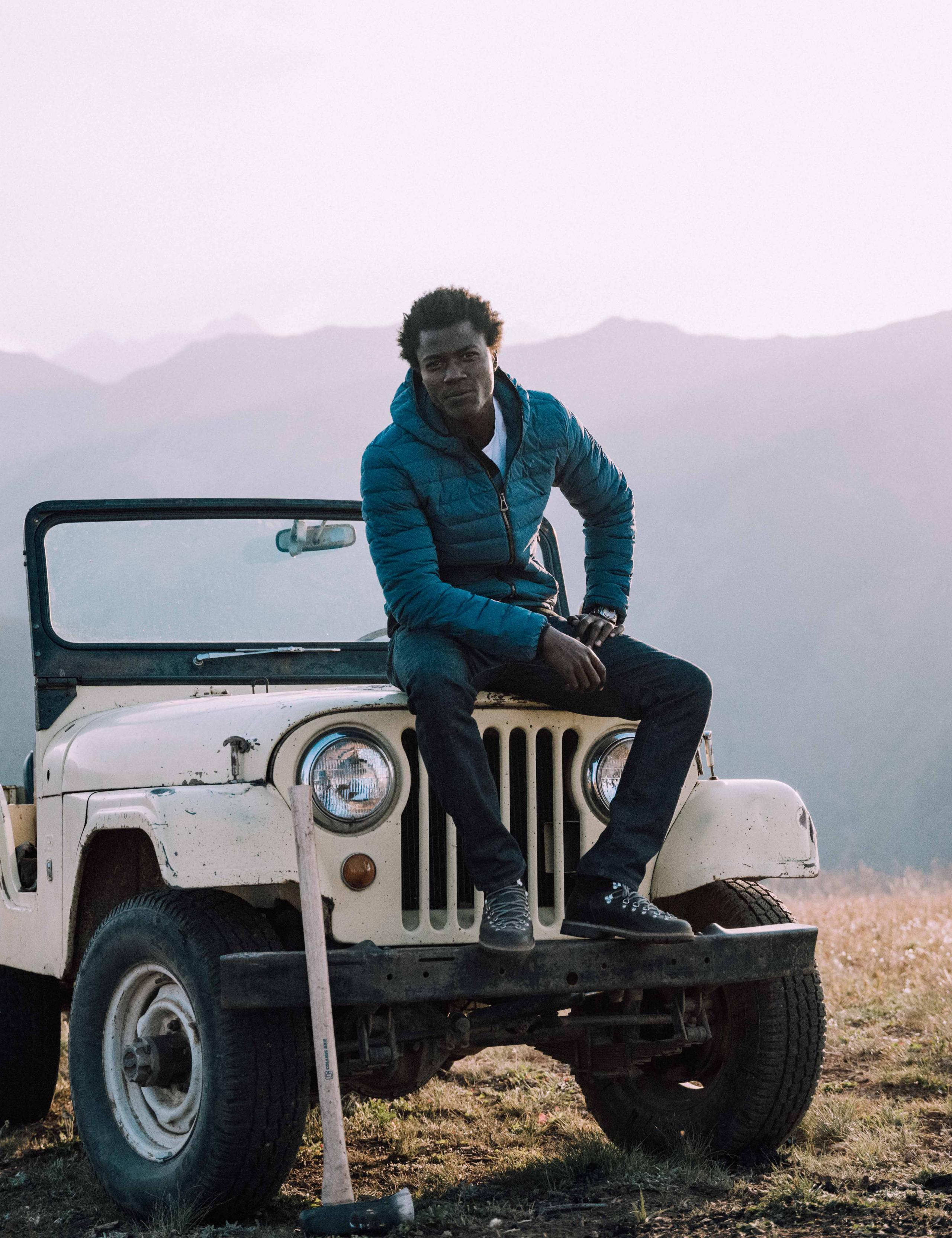 Man sitting on front of vintage Jeep with Aspen mountains in background