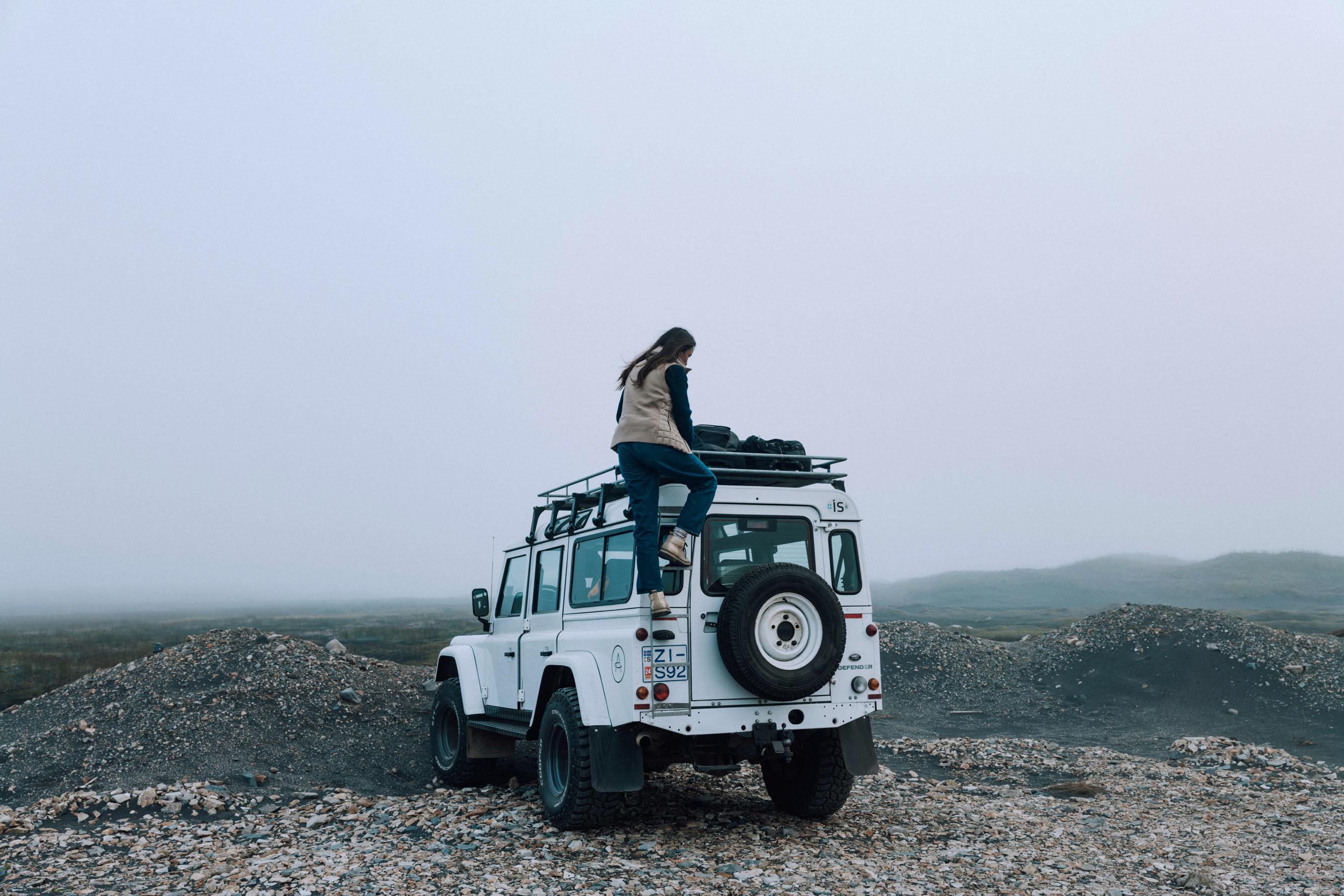 Woman climbing up back of white Defender truck to get luggage from the roof