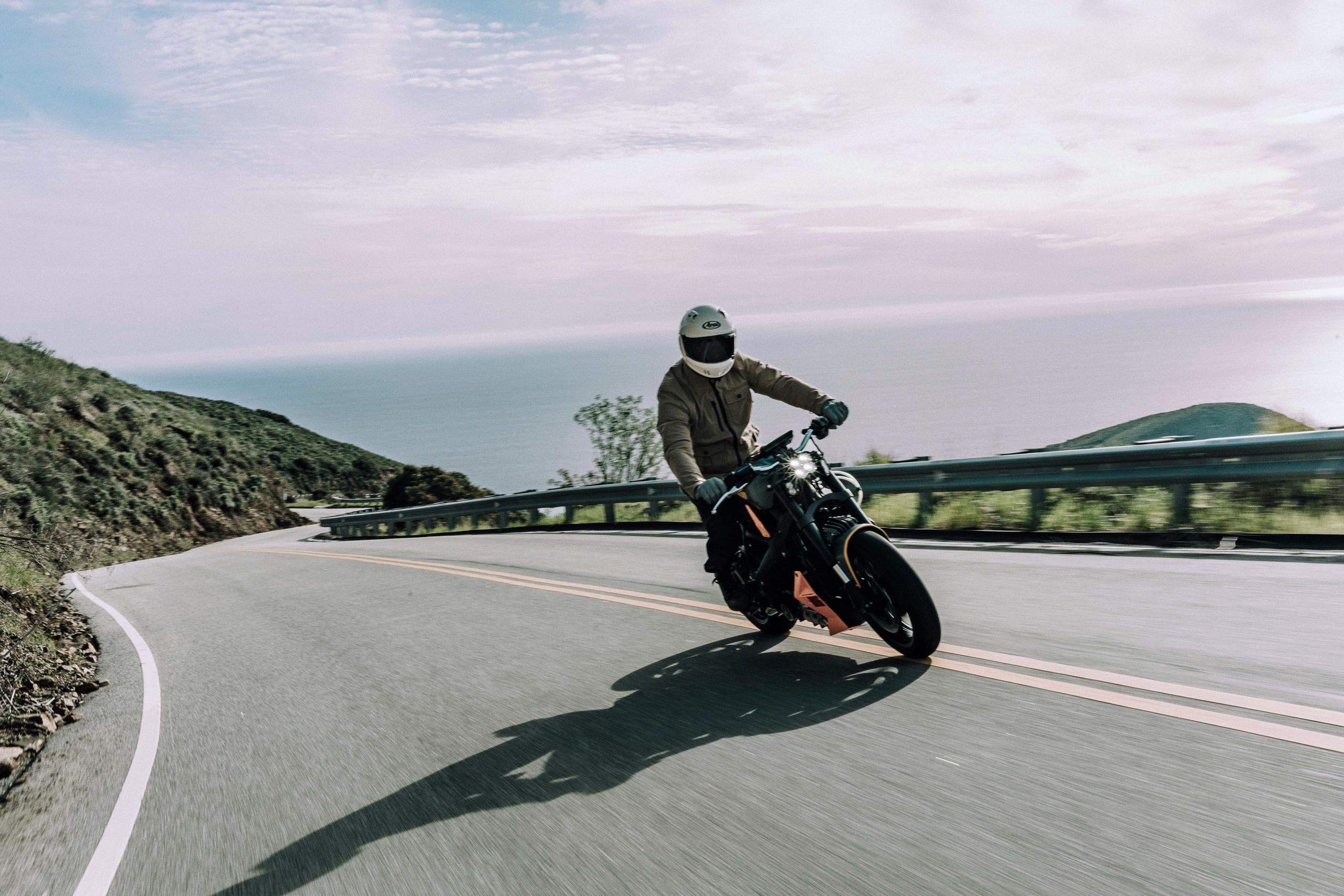 Motorcyclist riding up hills in Malibu with Pacific Ocean in the background
