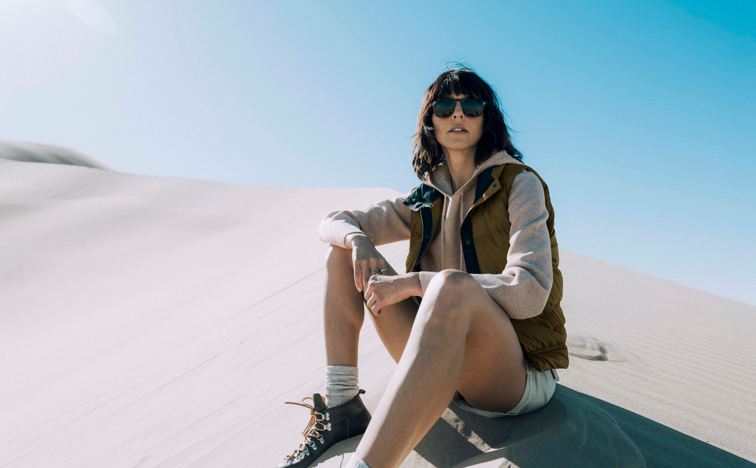 Woman wearing Sequoia sunglasses sitting on sand dunes