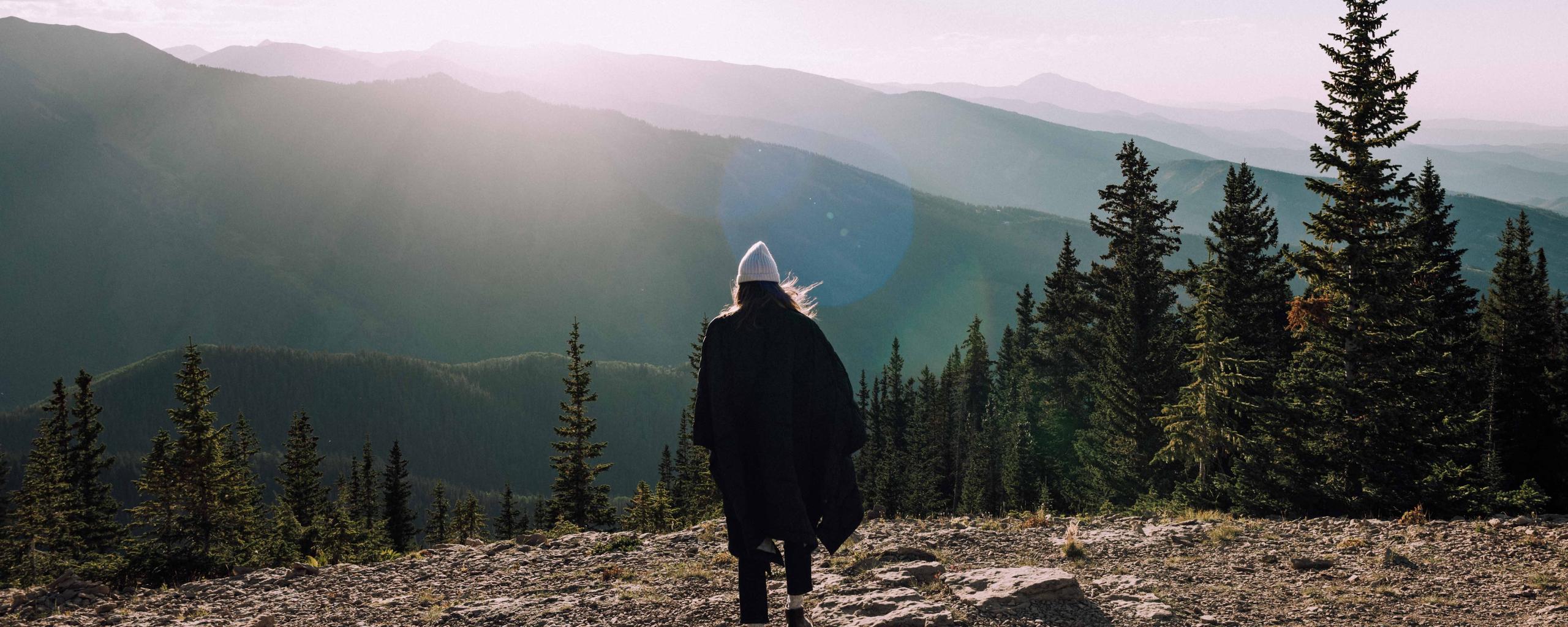 Woman walking on mountain terrain towards sunset light in Colorado