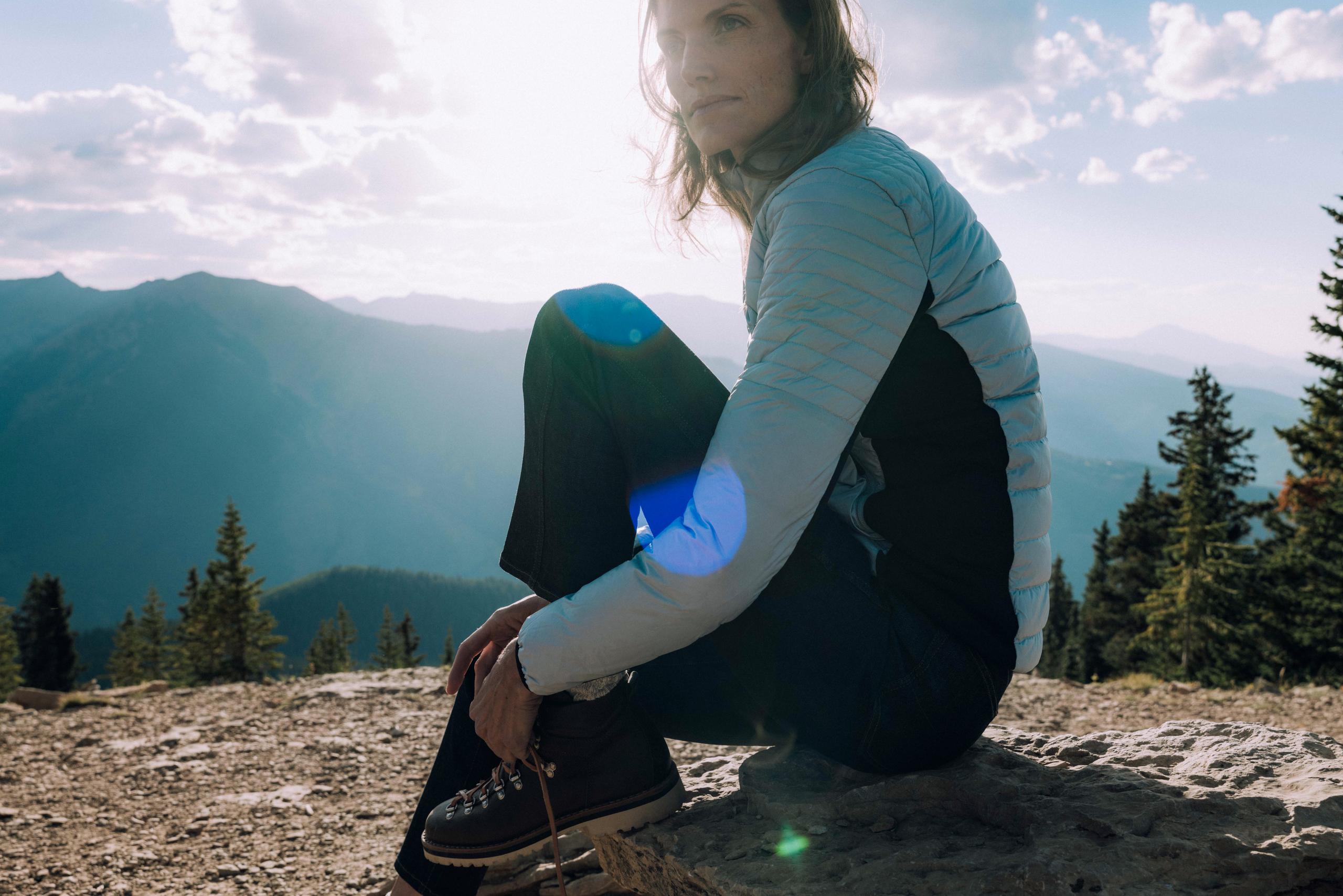 Profile of woman sitting on rock tying her shoelaces in front of Aspen mountains