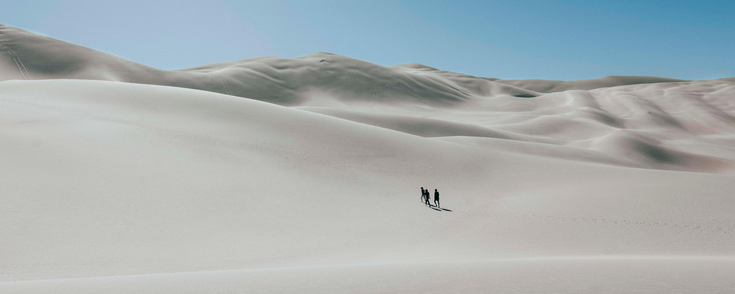 Three people walking on sand dunes in the distance