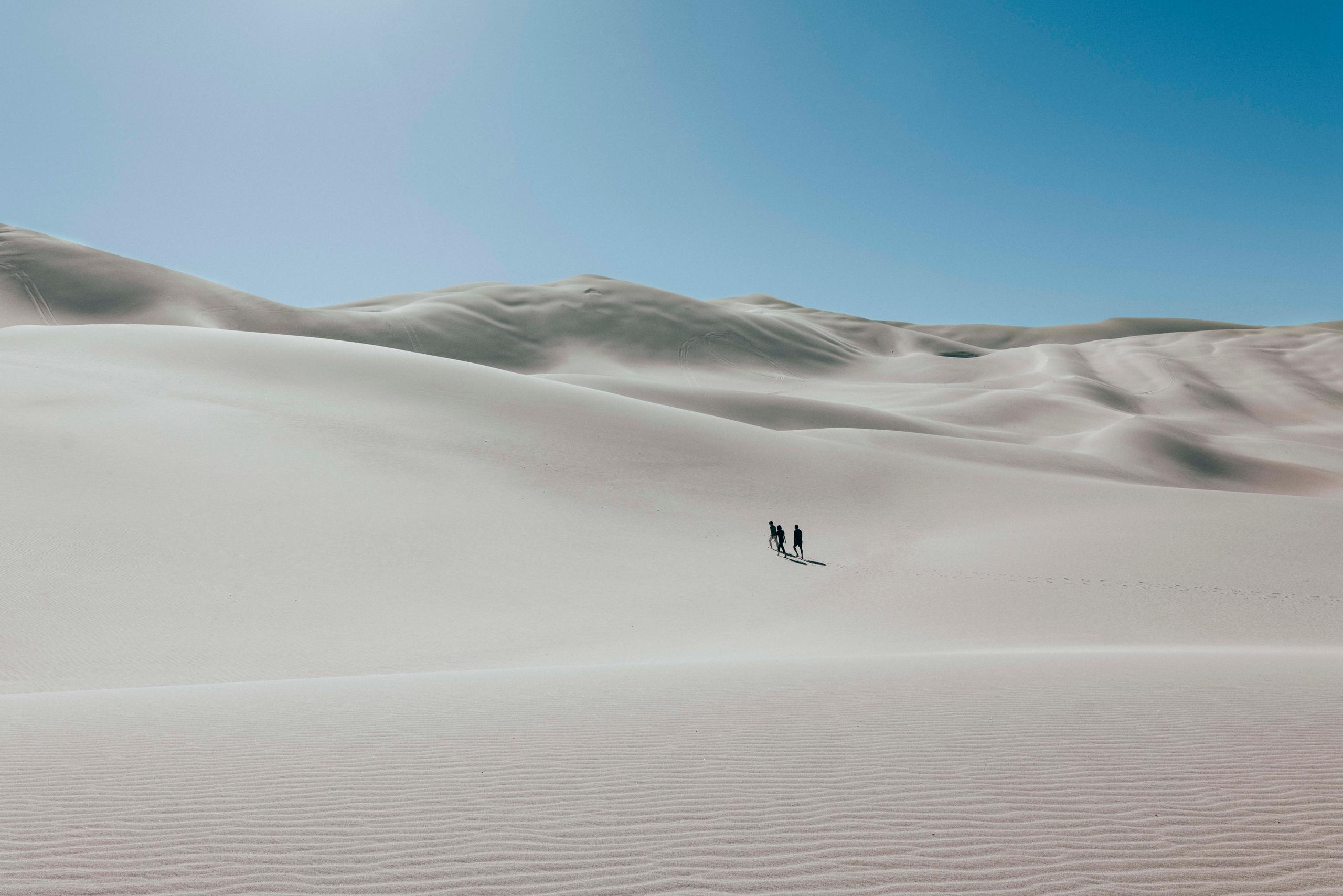Three people walking in the distance on vast sand dunes landscape