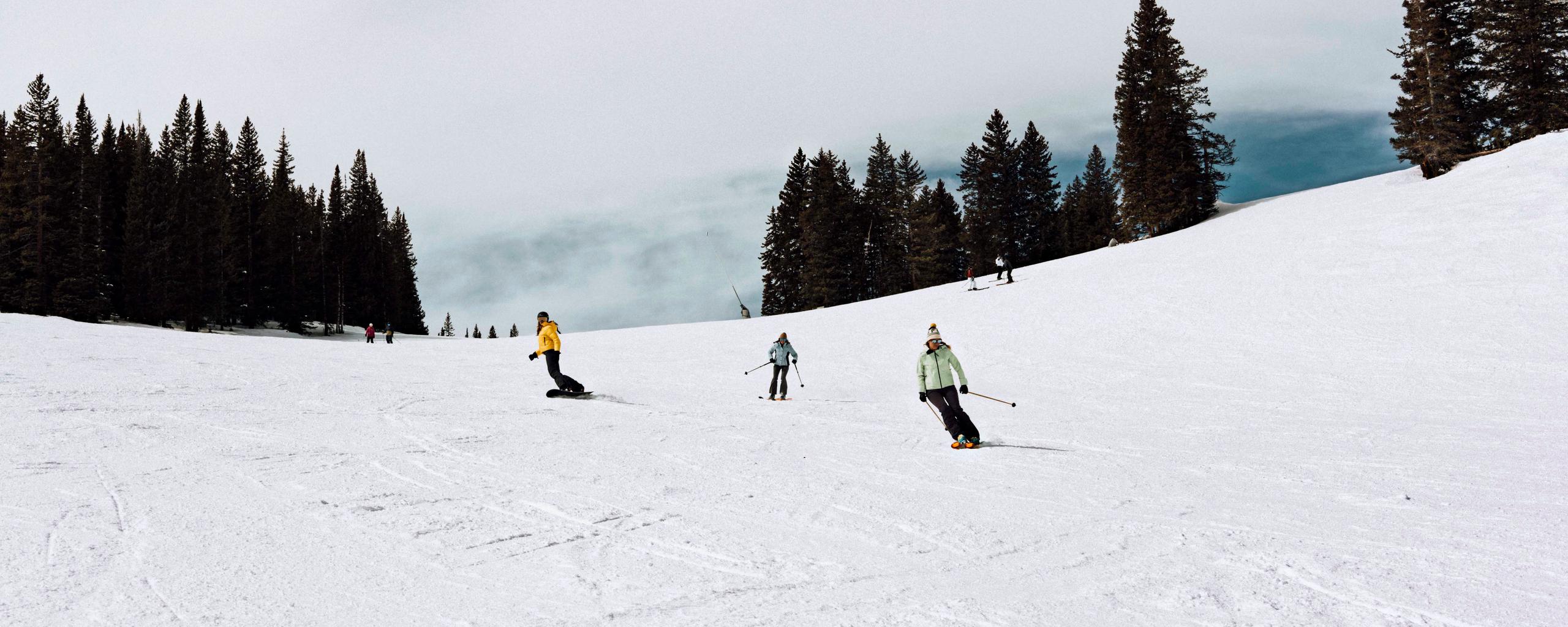 Female snowboarder and skiiers riding down the mountain in Aspen