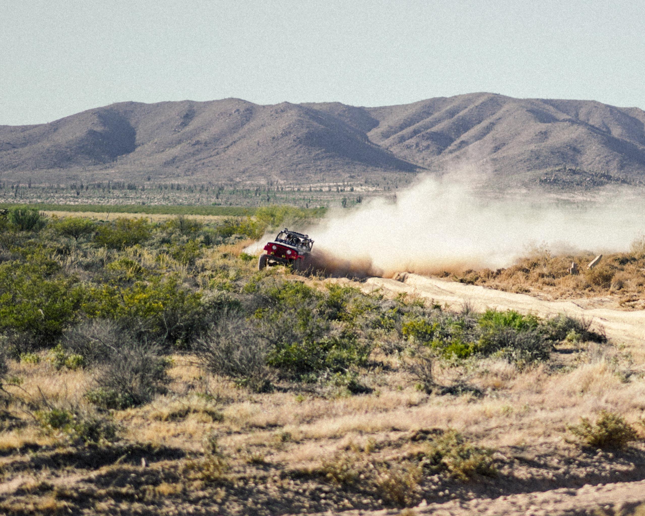 1969 Jeep Commando driving on dirt road in desert landscape kicking up plumes of dust 