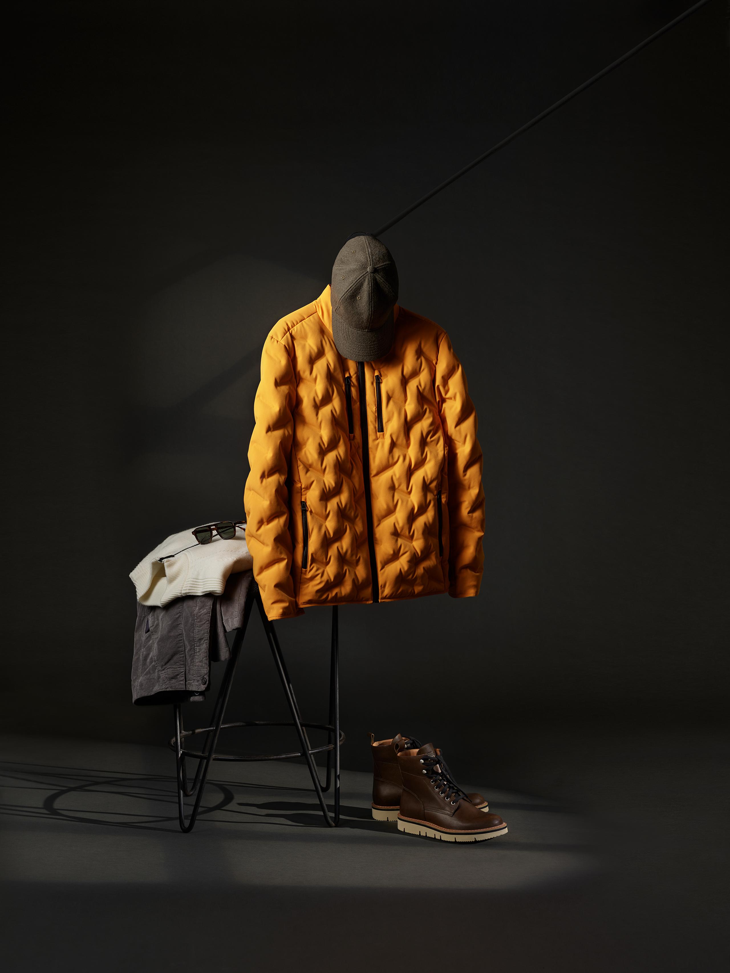 Studio setup of AETHER men's outfit hanging and resting on chair against black background