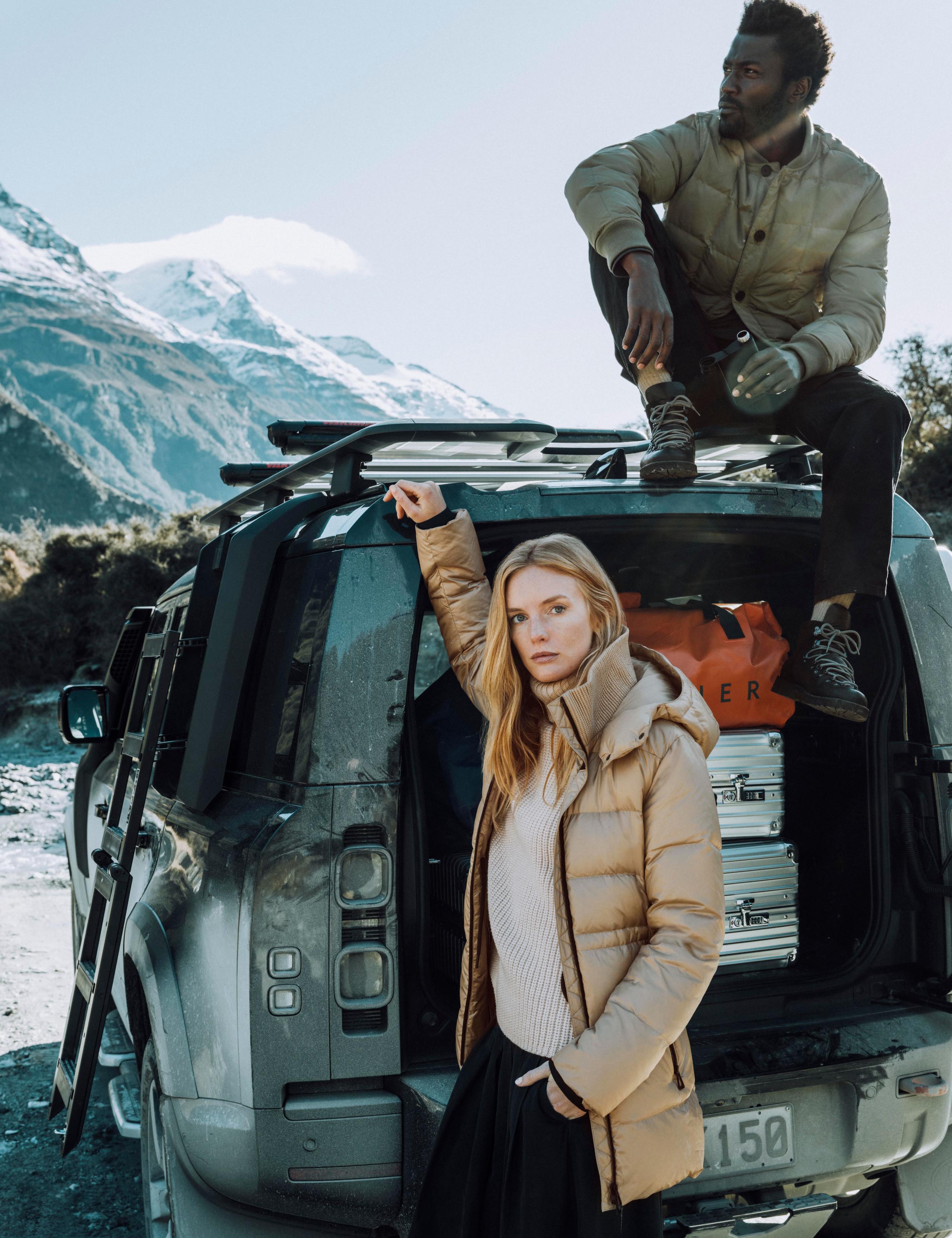 Woman and man hanging along outside of Defender in New Zealand landscape