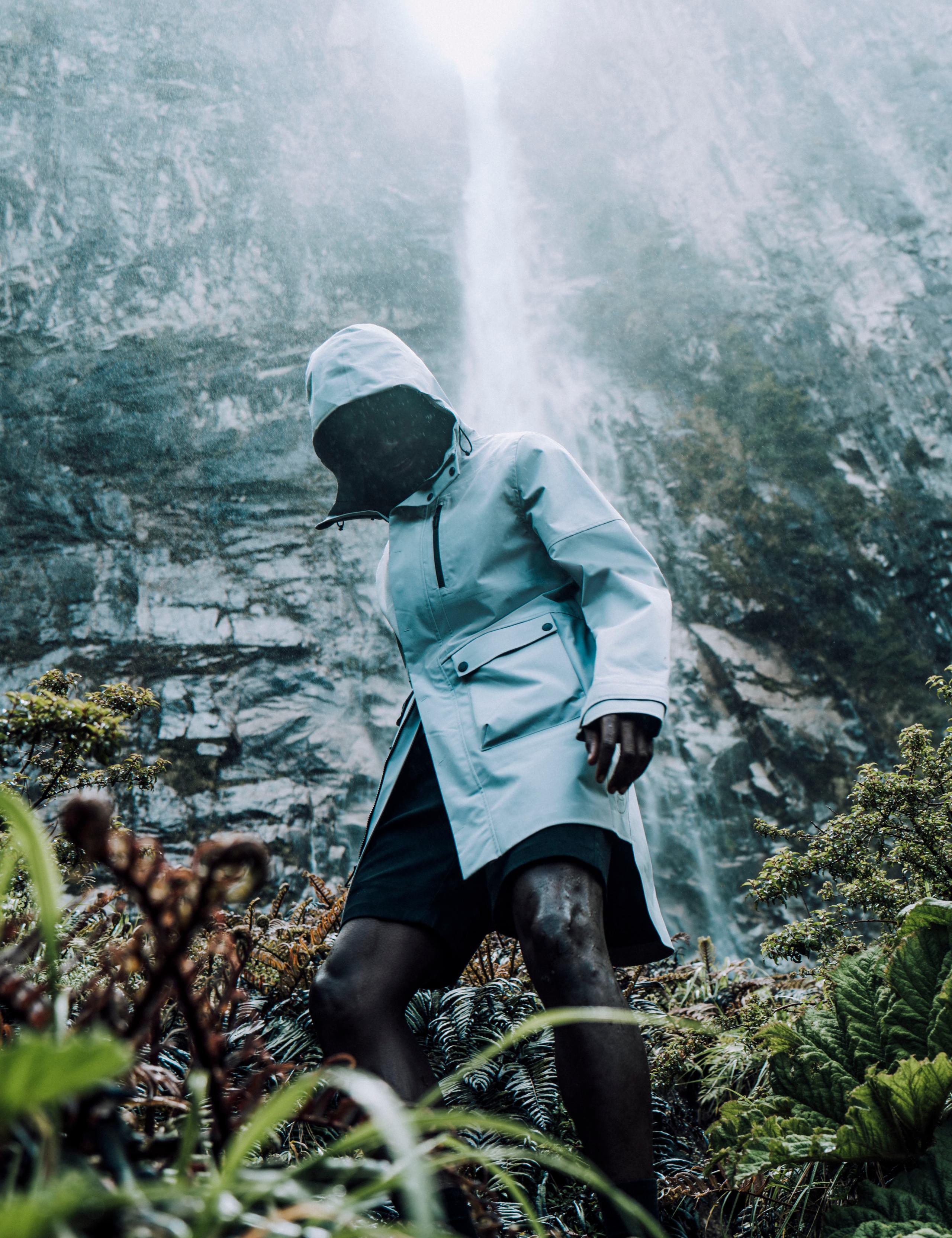 Man in Anders Rain Jacket walking through forest with waterfall in background in Patagonia