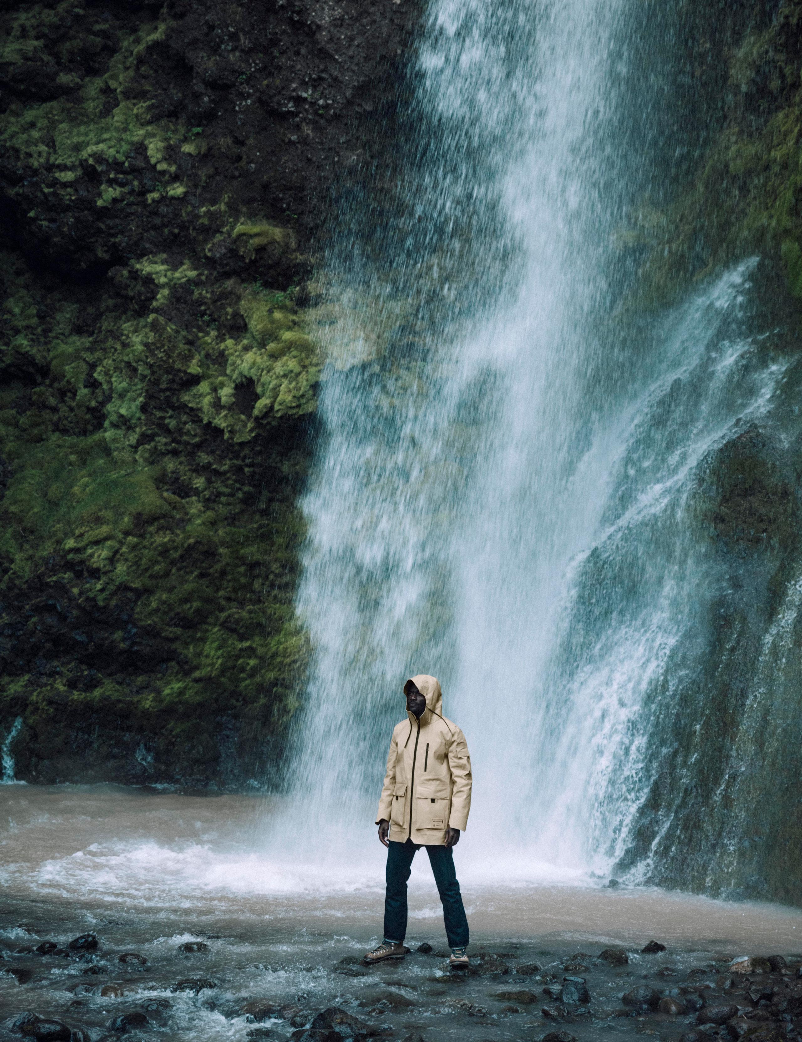 Man wearing AETHER + Mackintosh Field Parka next to waterfall in Iceland