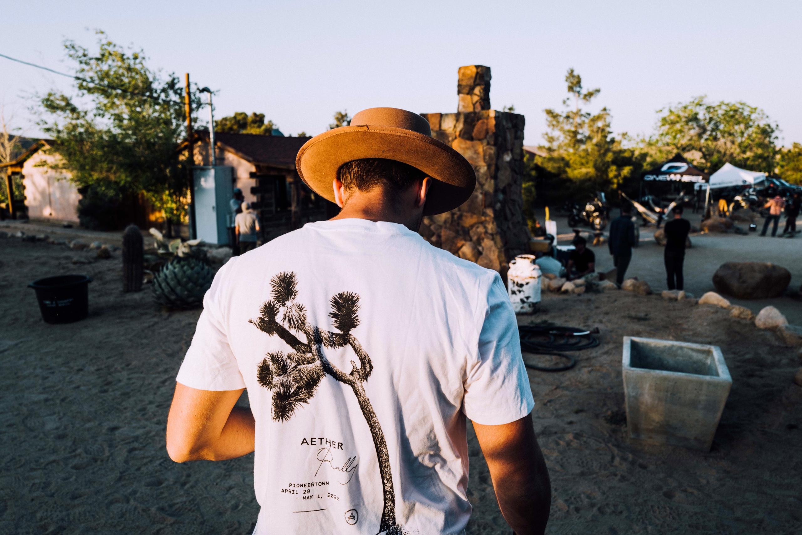 Man in hat and white AETHER shirt walking through AETHER Rally in Joshua Tree, California