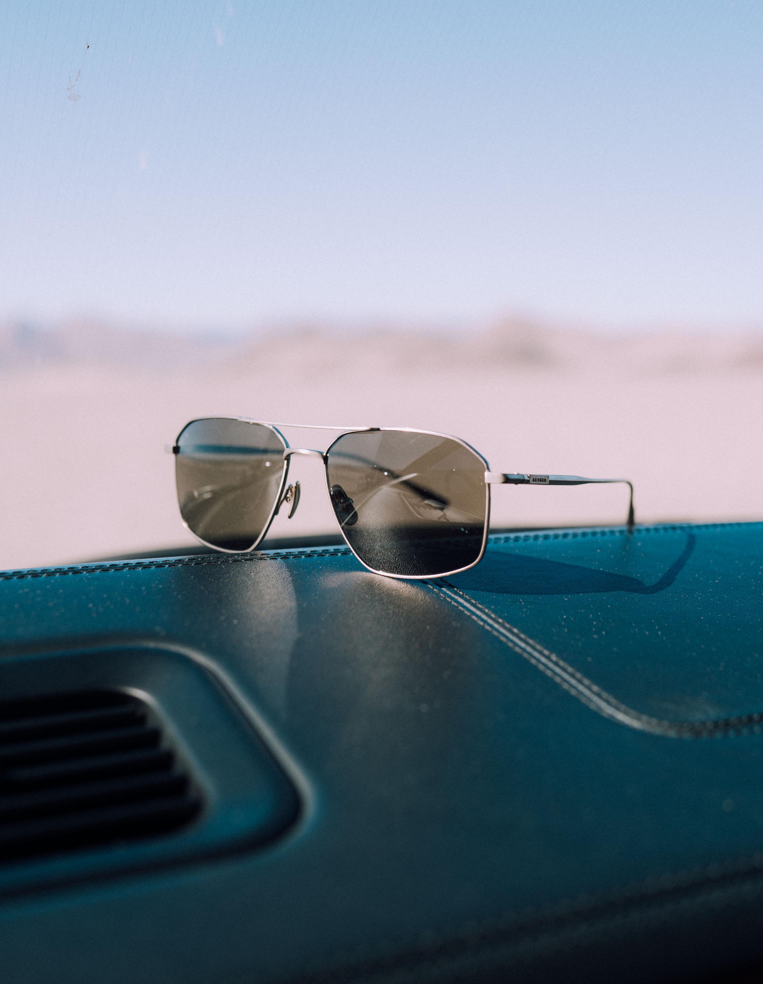 Arches sunglass sitting on dashboard of car with sand dunes in the background