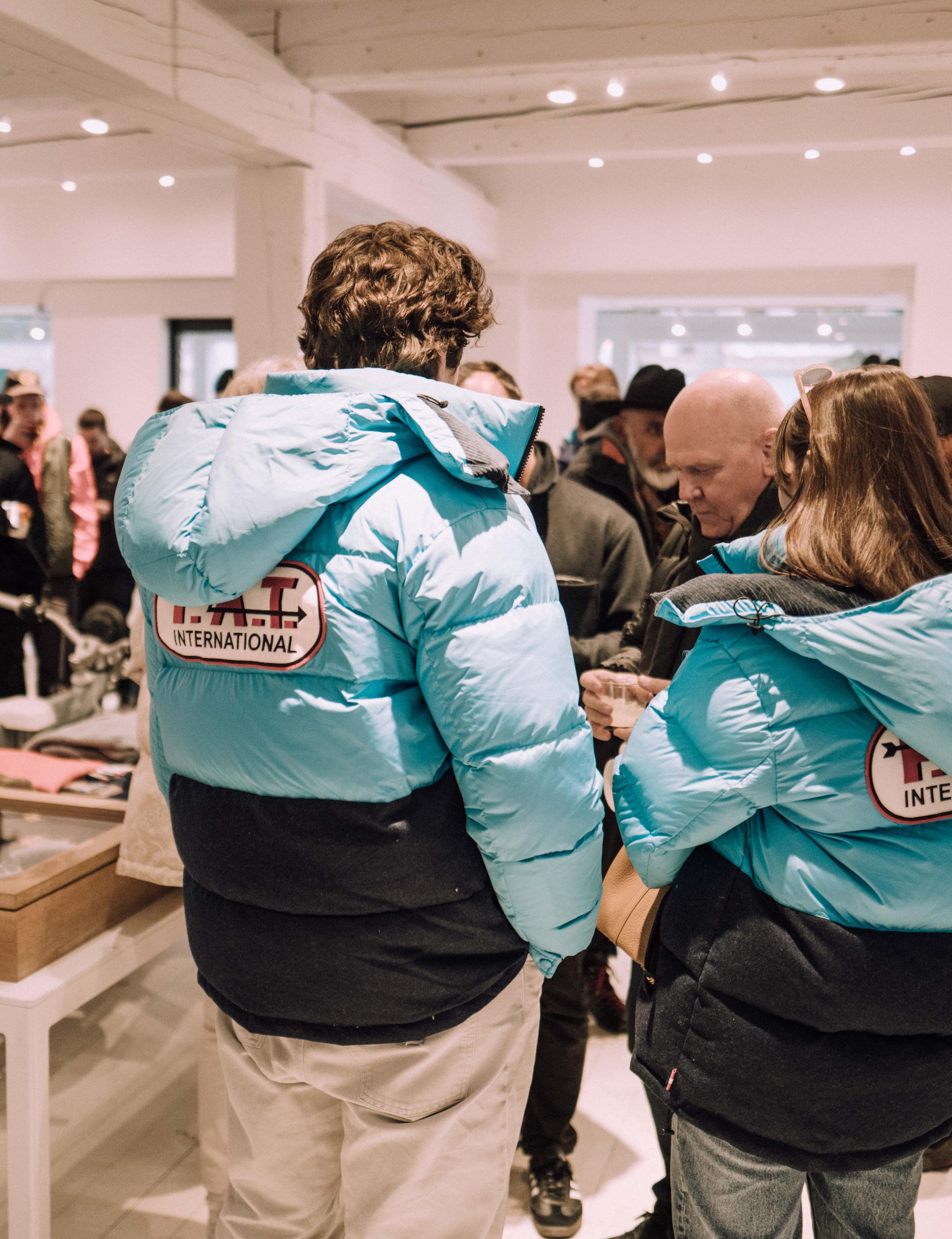 Two people wearing sky blue F.A.T. snow jackets inside Aether Aspen store party