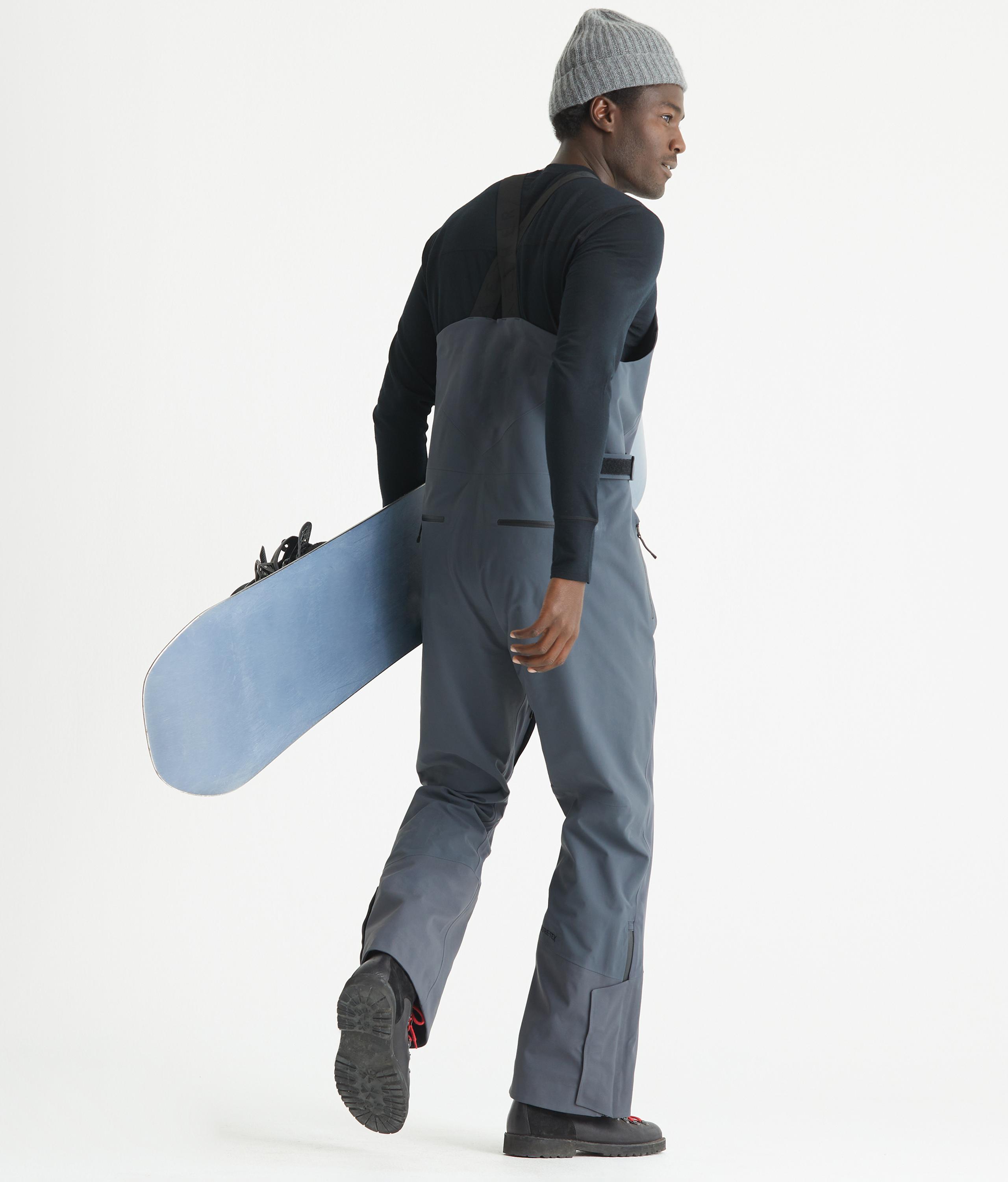 Man wearing Stealth Snow Bib holding snowboard in studio