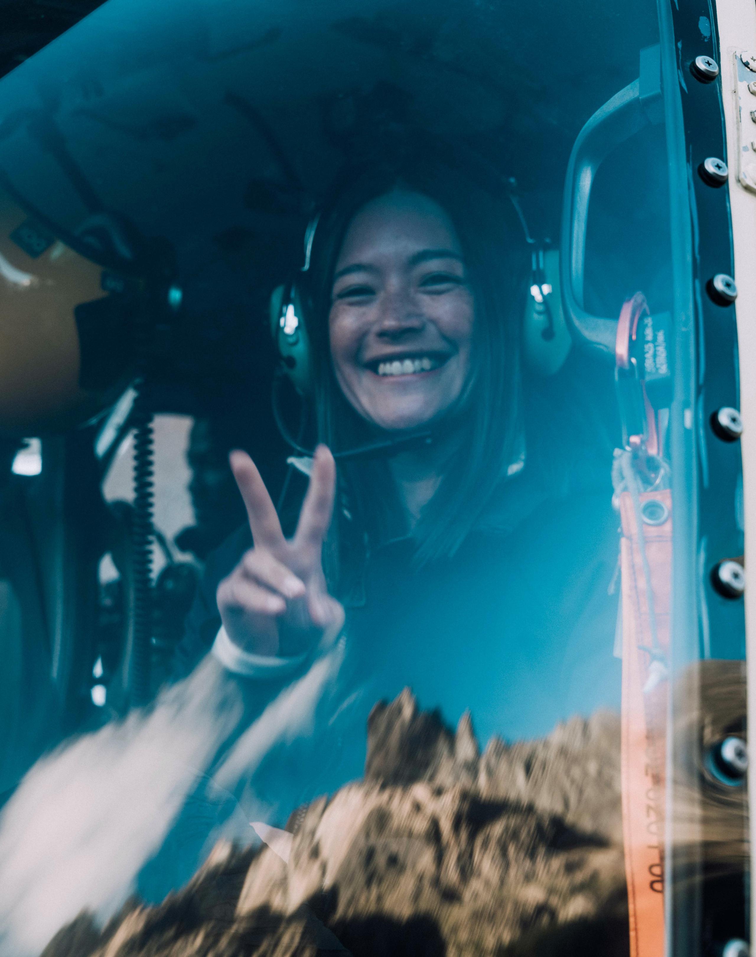 Woman giving peace sign and smiling from inside helicopter