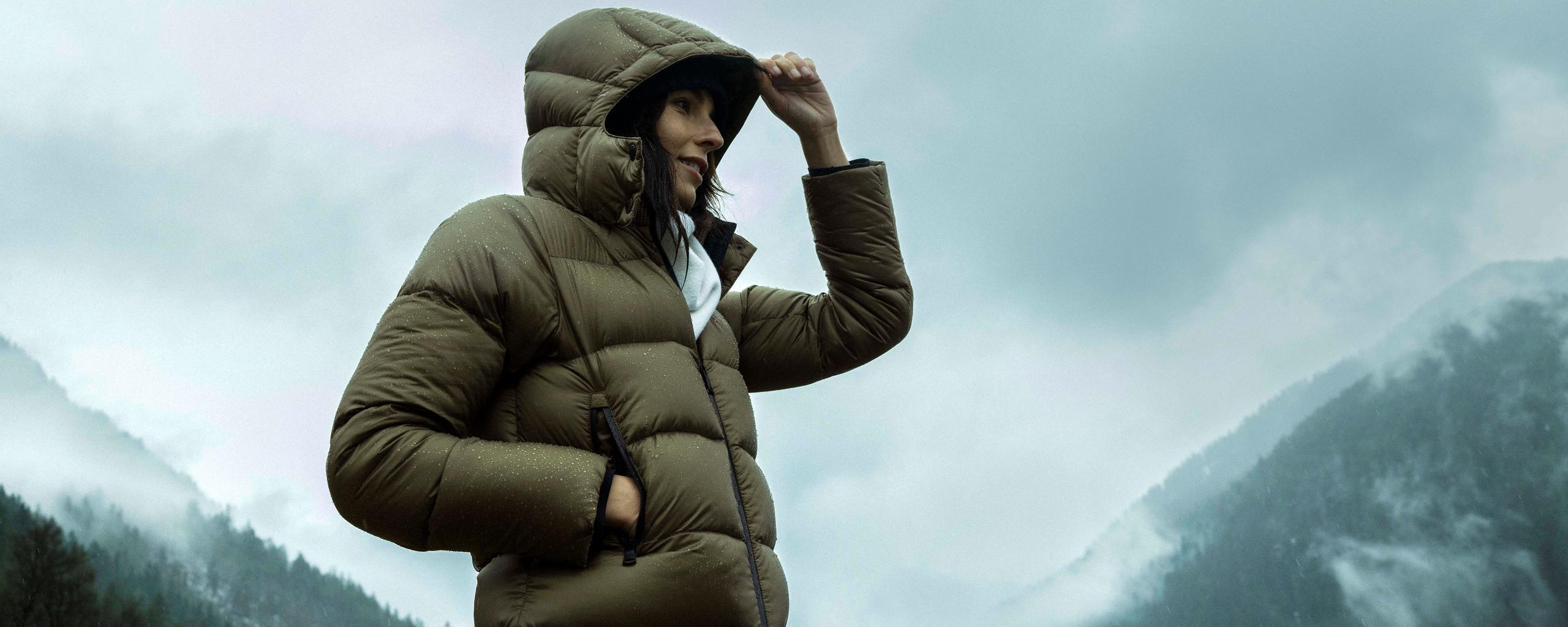 Woman wearing hooded jacket in light rain in front of foggy mountains in the French Alps