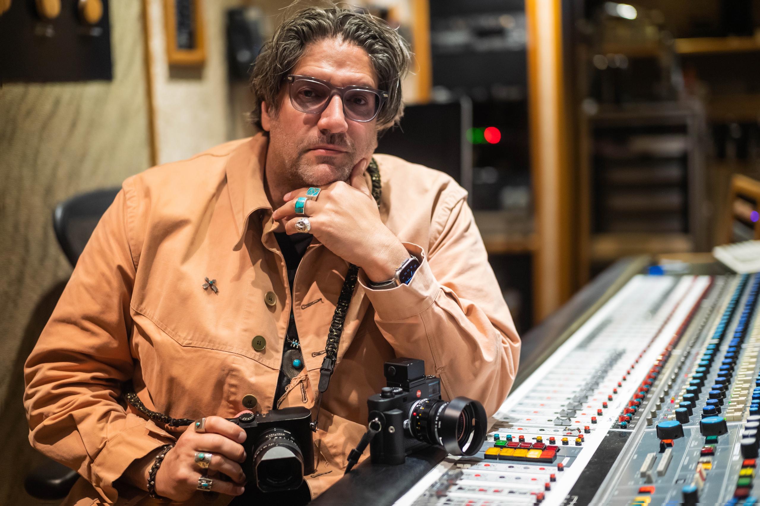 Mathieu Bitton holding Leica camera sitting at studio mixing board